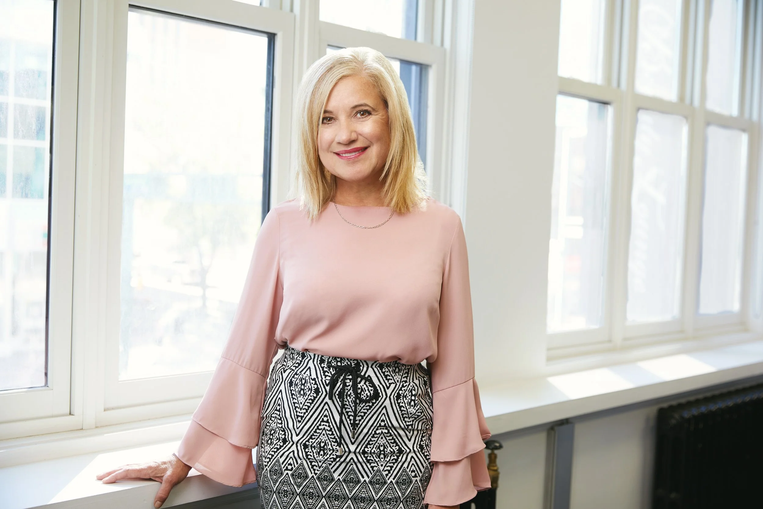 Office portrait standing at a bright window, pink blouse