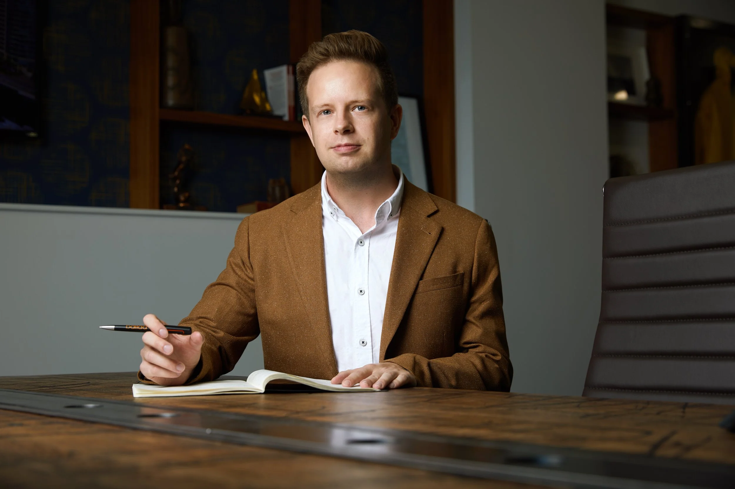 Office portrait at a boardroom table with a notebook, brown jacket