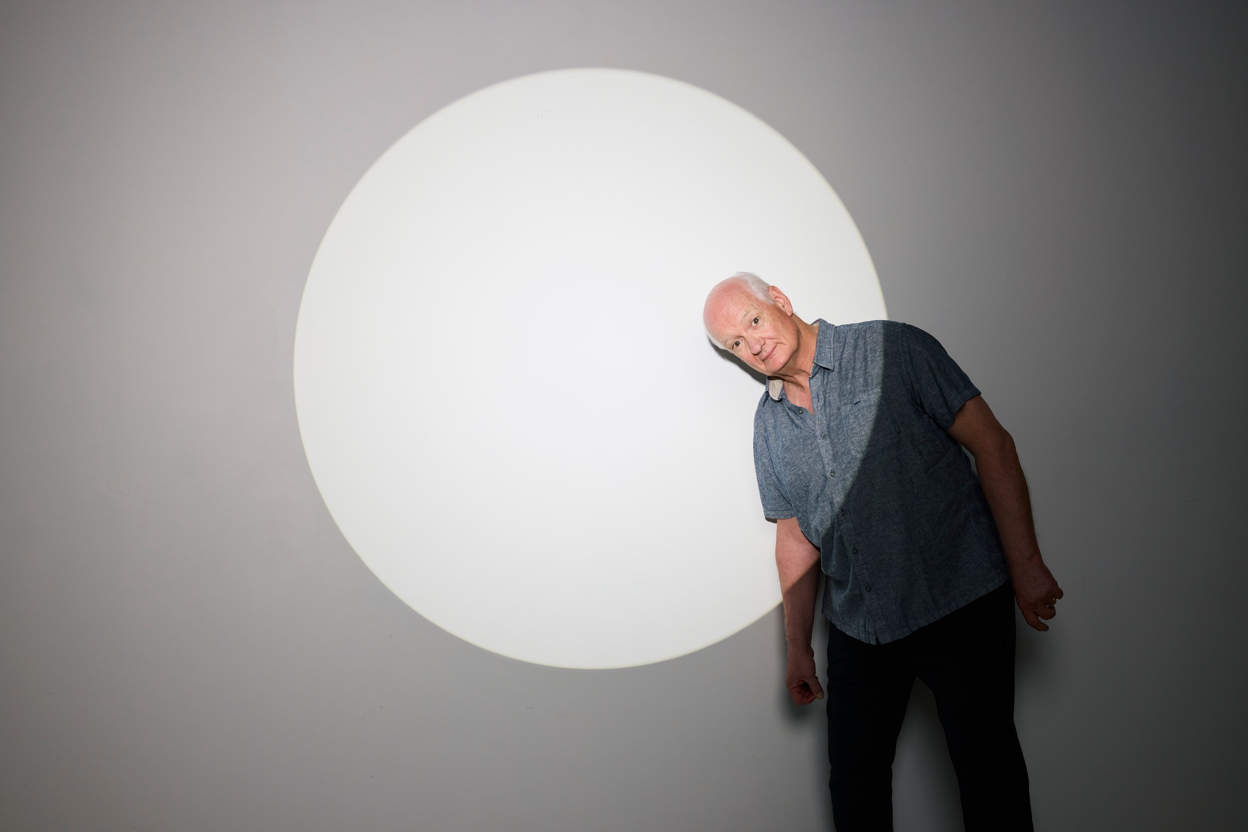 Colin Mochrie leaning into a circle of white light on grey, for Colin Mochrie Live