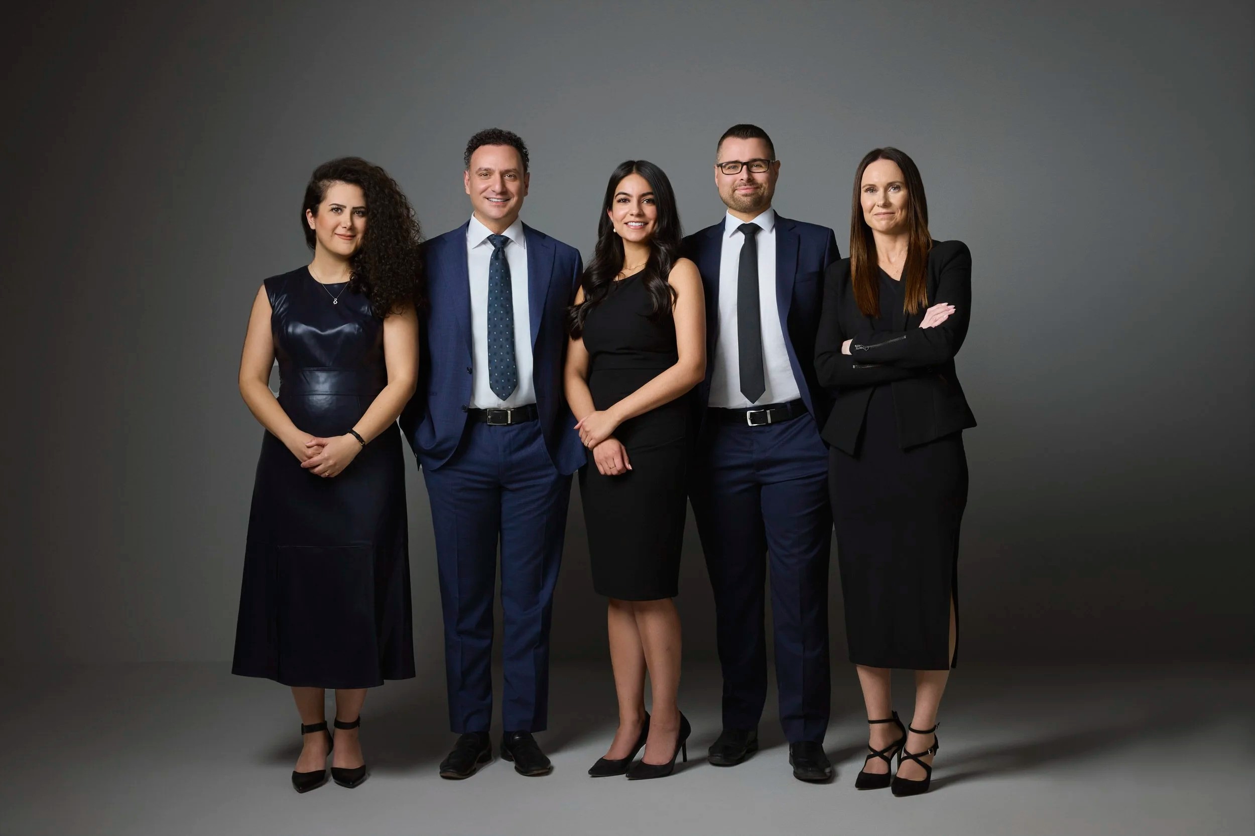 Group photo of a five-person team in dark suits on grey, Edmonton studio