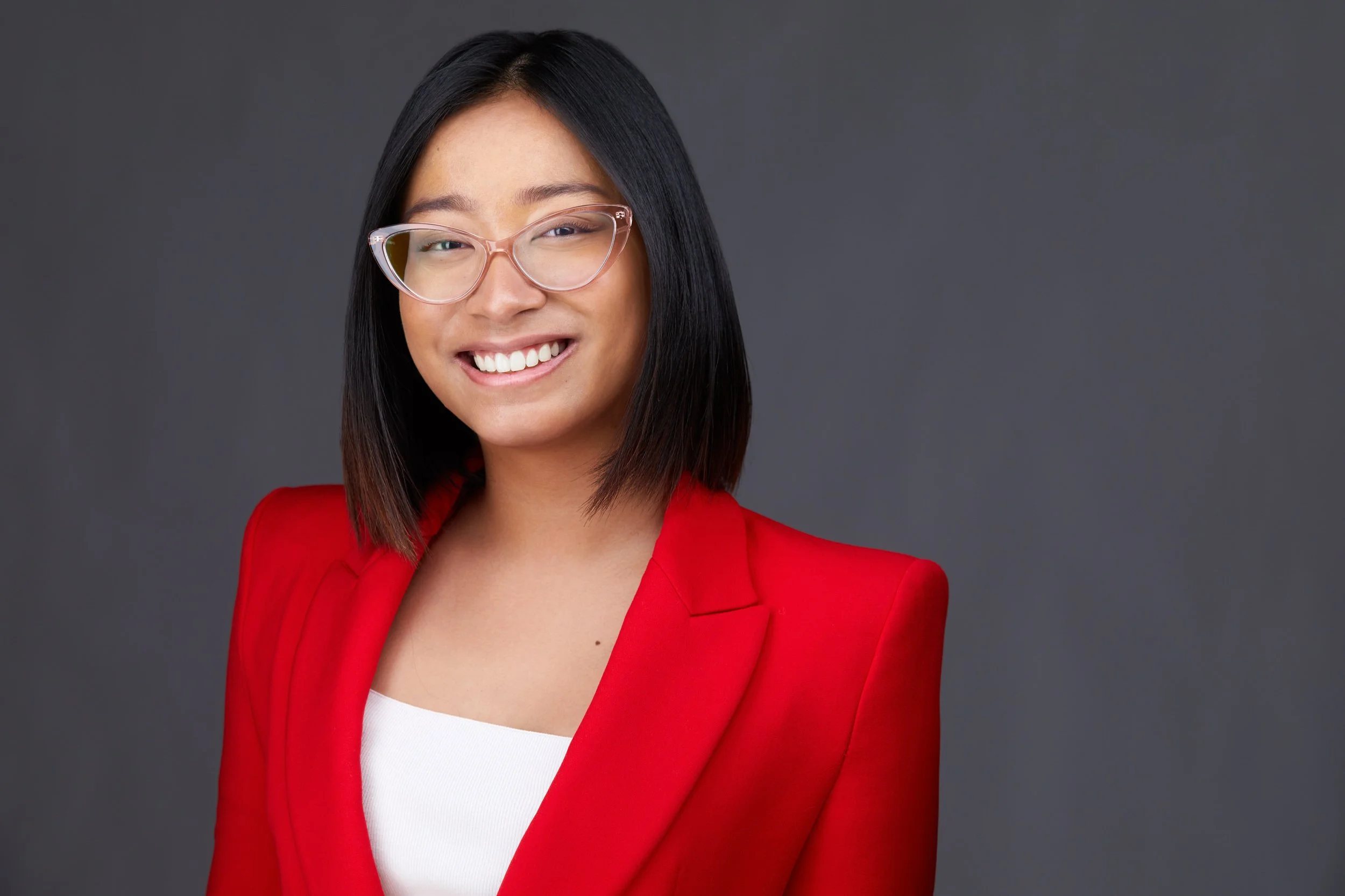 Rajah Maggay, corporate headshot in a red blazer on a charcoal backdrop, Edmonton
