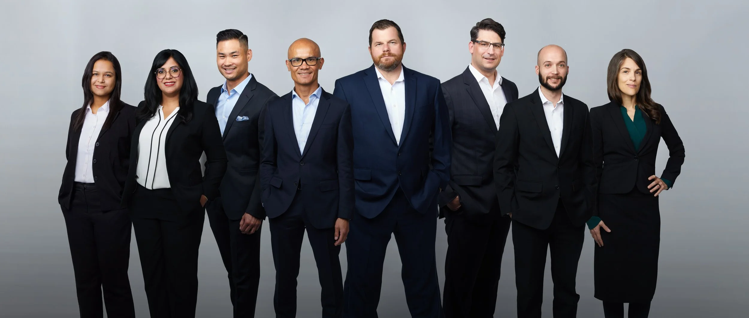 A team of seven in a line, photographed together on a dark grey backdrop