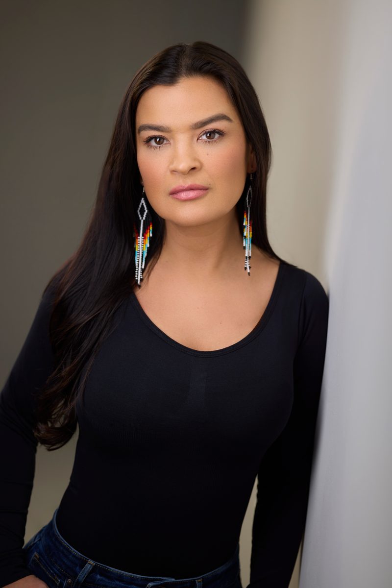 Crystle Lightning in a black top and beaded earrings against grey