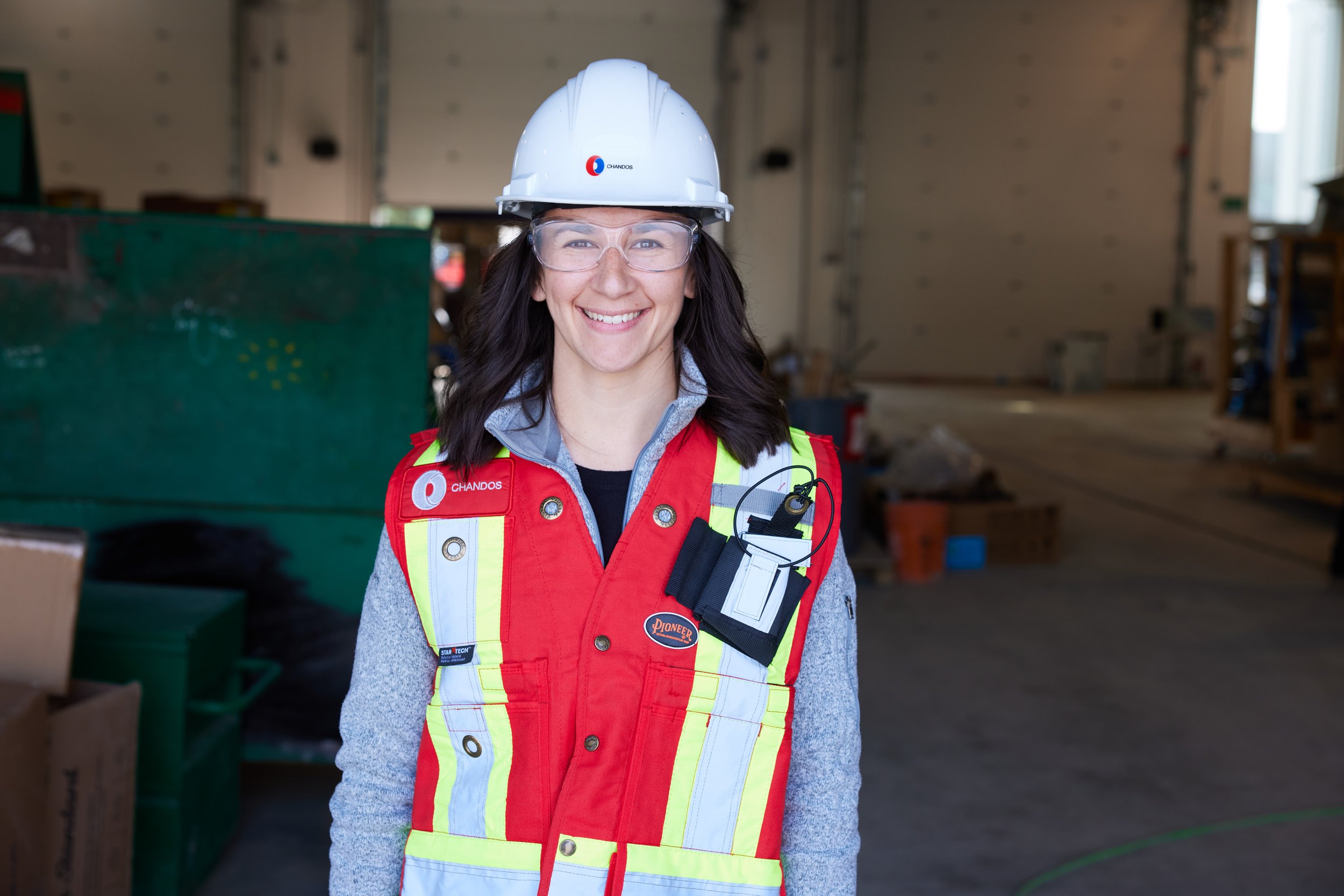 A smiling woman in a hard hat in an open warehouse