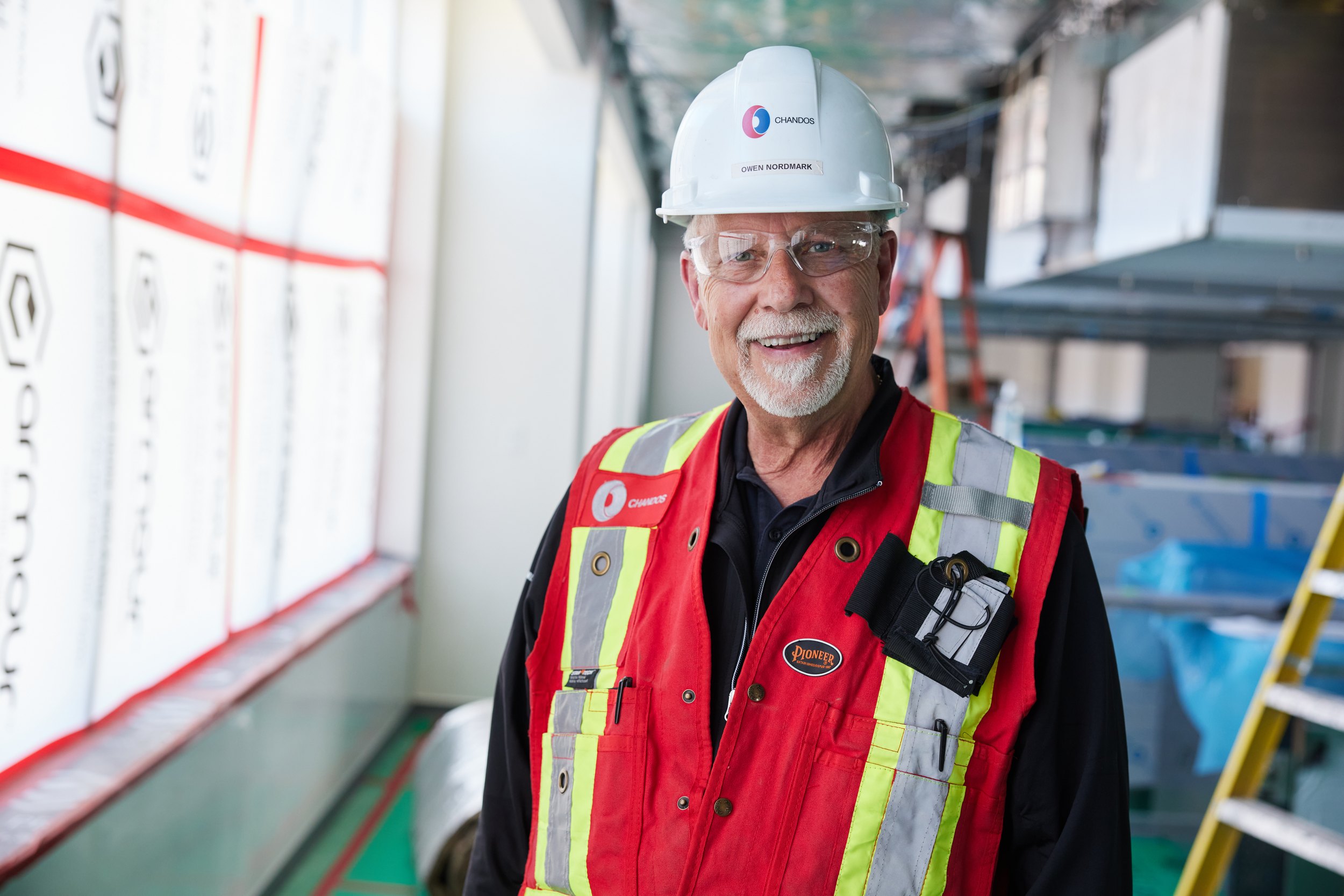 A smiling man in a hard hat and vest by a window
