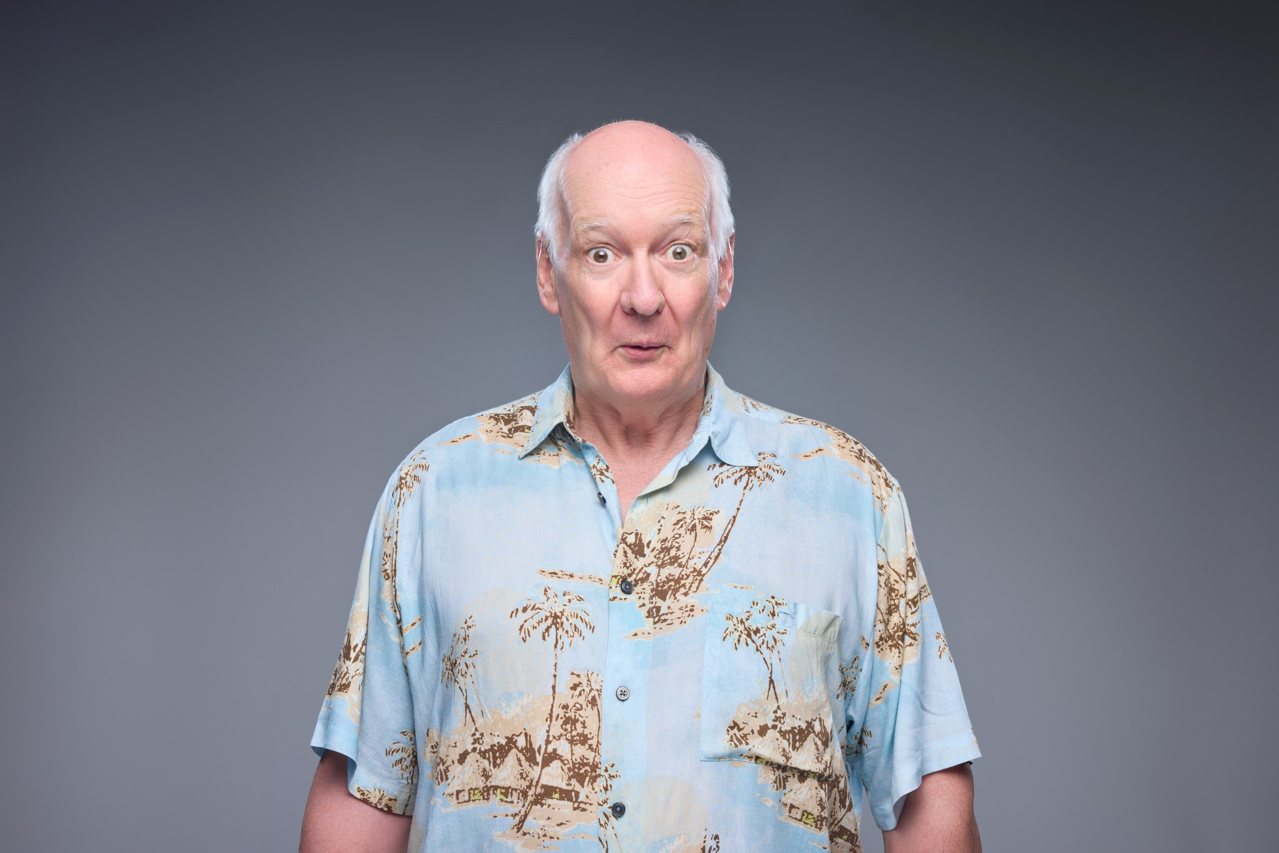 Colin Mochrie in the palm-print shirt, eyebrows up and mouth open, against grey