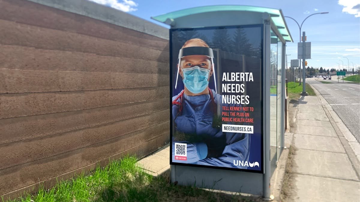 A United Nurses of Alberta “Alberta Needs Nurses” poster in a bus shelter beside a street, by day