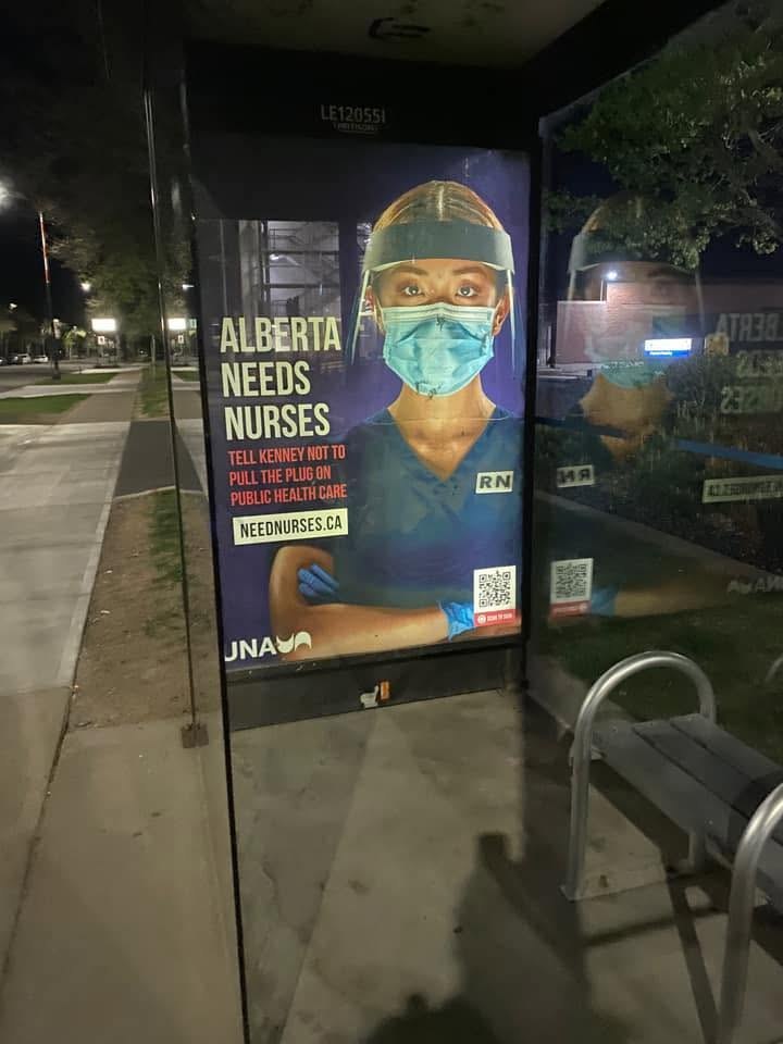 The same United Nurses of Alberta poster lit up in a bus shelter at night