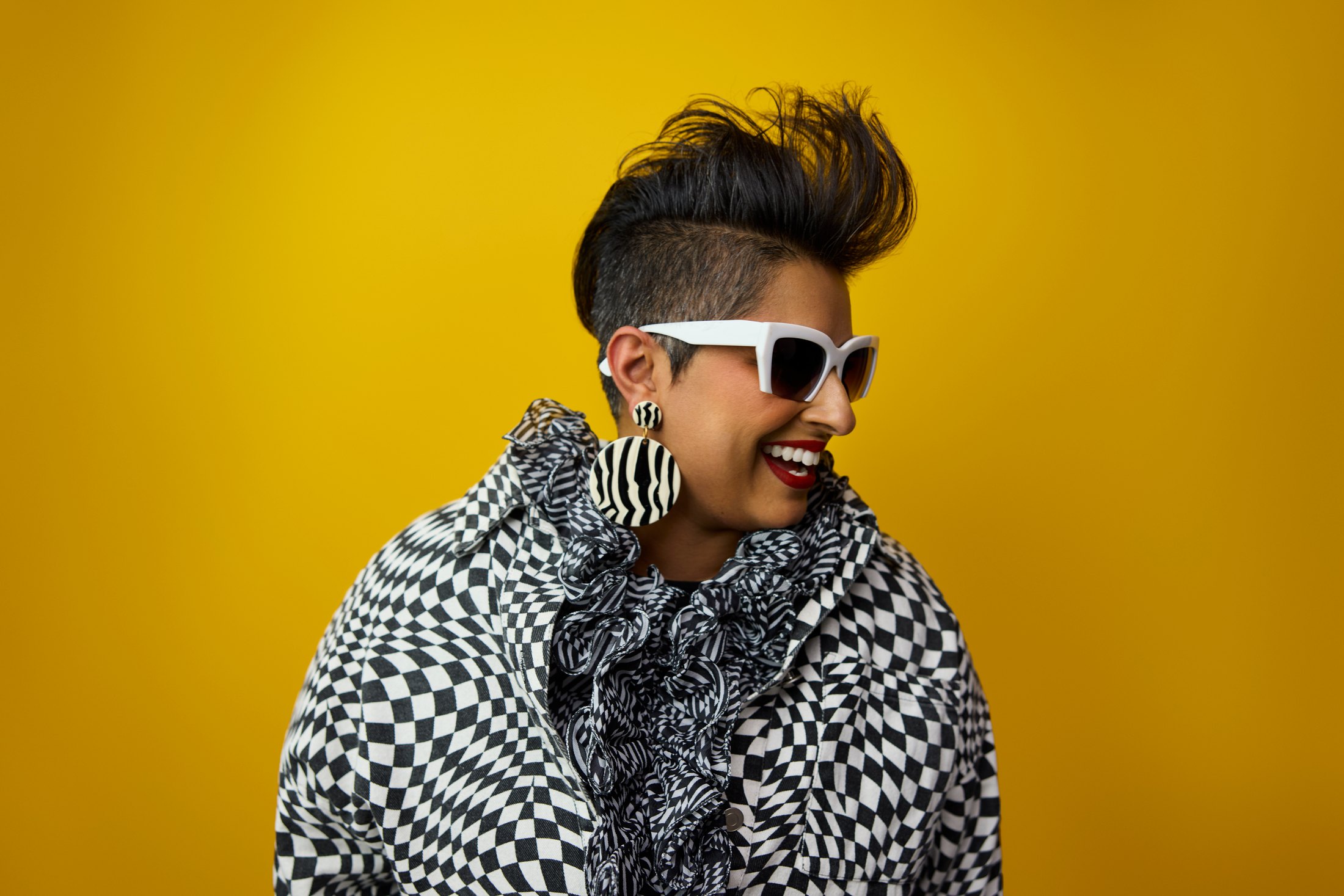 A woman in a houndstooth coat and white sunglasses against gold