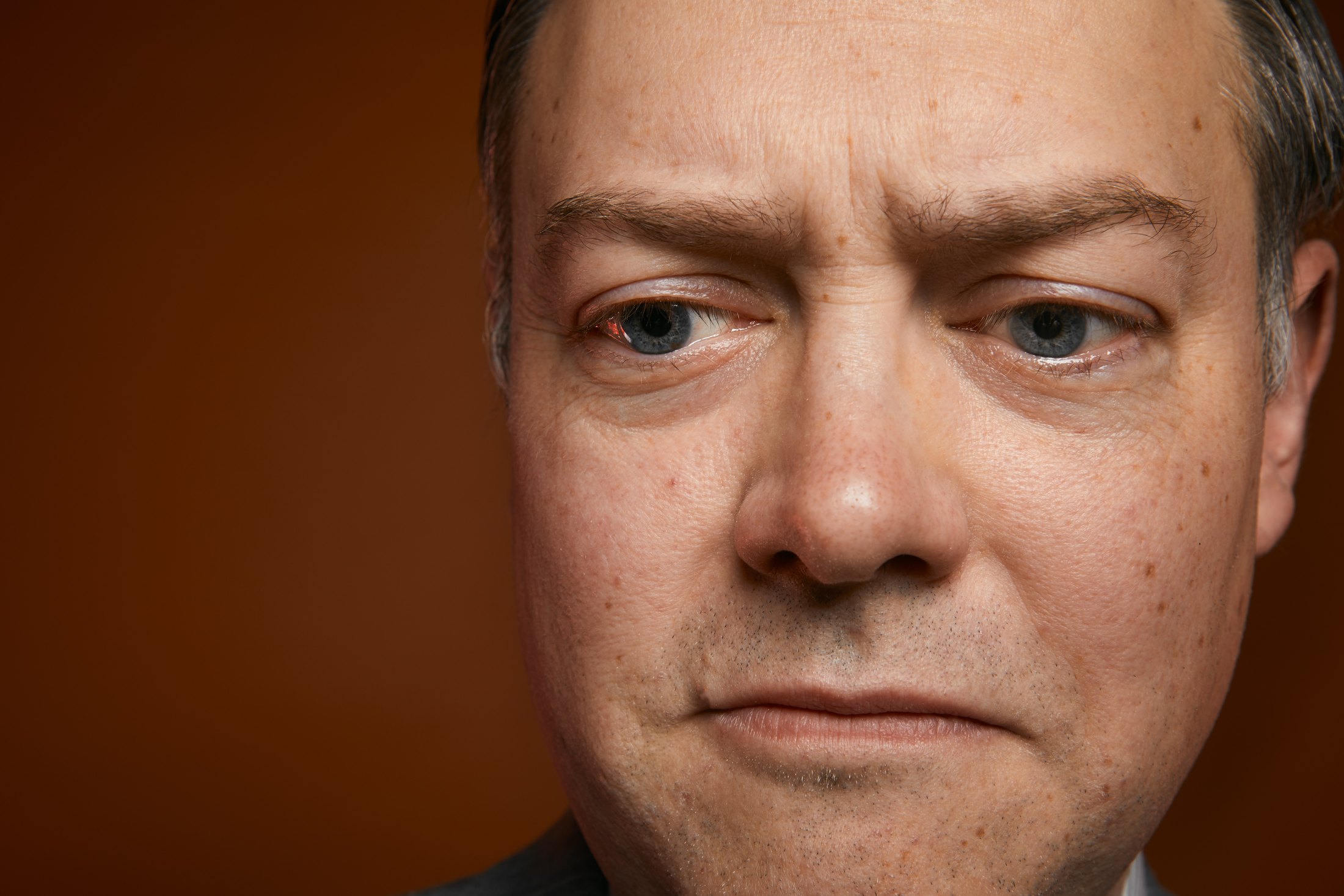 A man’s face filling the frame against rust, holding the camera’s eye