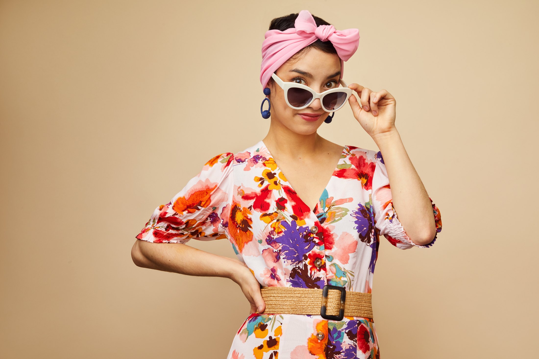 A performer in a floral dress, pink headwrap and white sunglasses, a hand on her hip