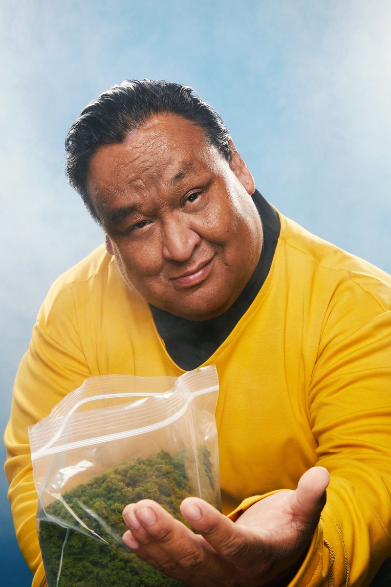 A performer in a yellow sweater holding out a clear bag against pale blue