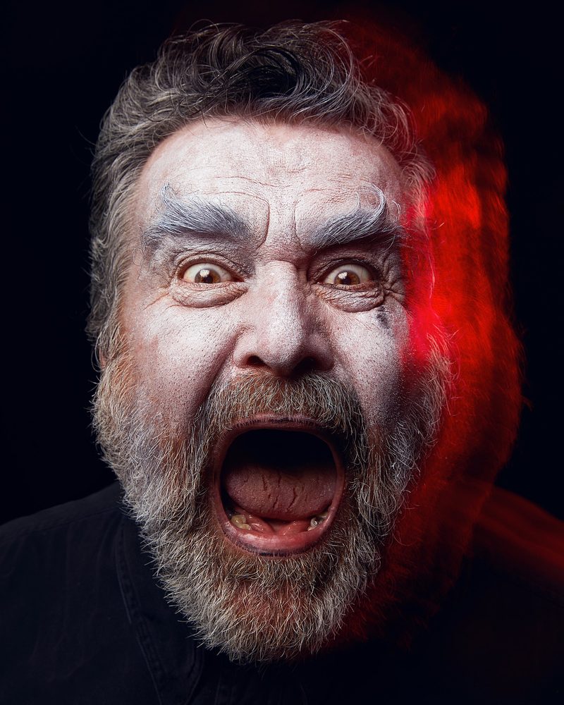 A bearded performer mid-shout, red light raking one side of his face