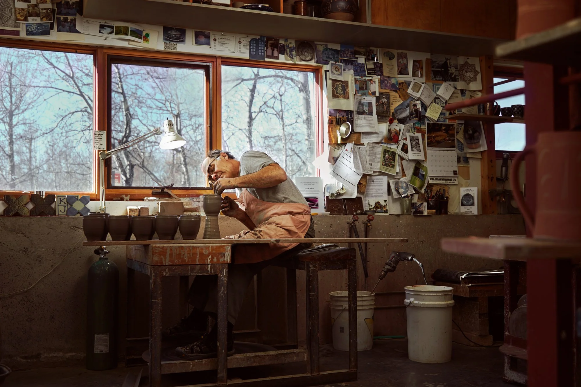 The same workshop from the door: the potter at the wheel by the window