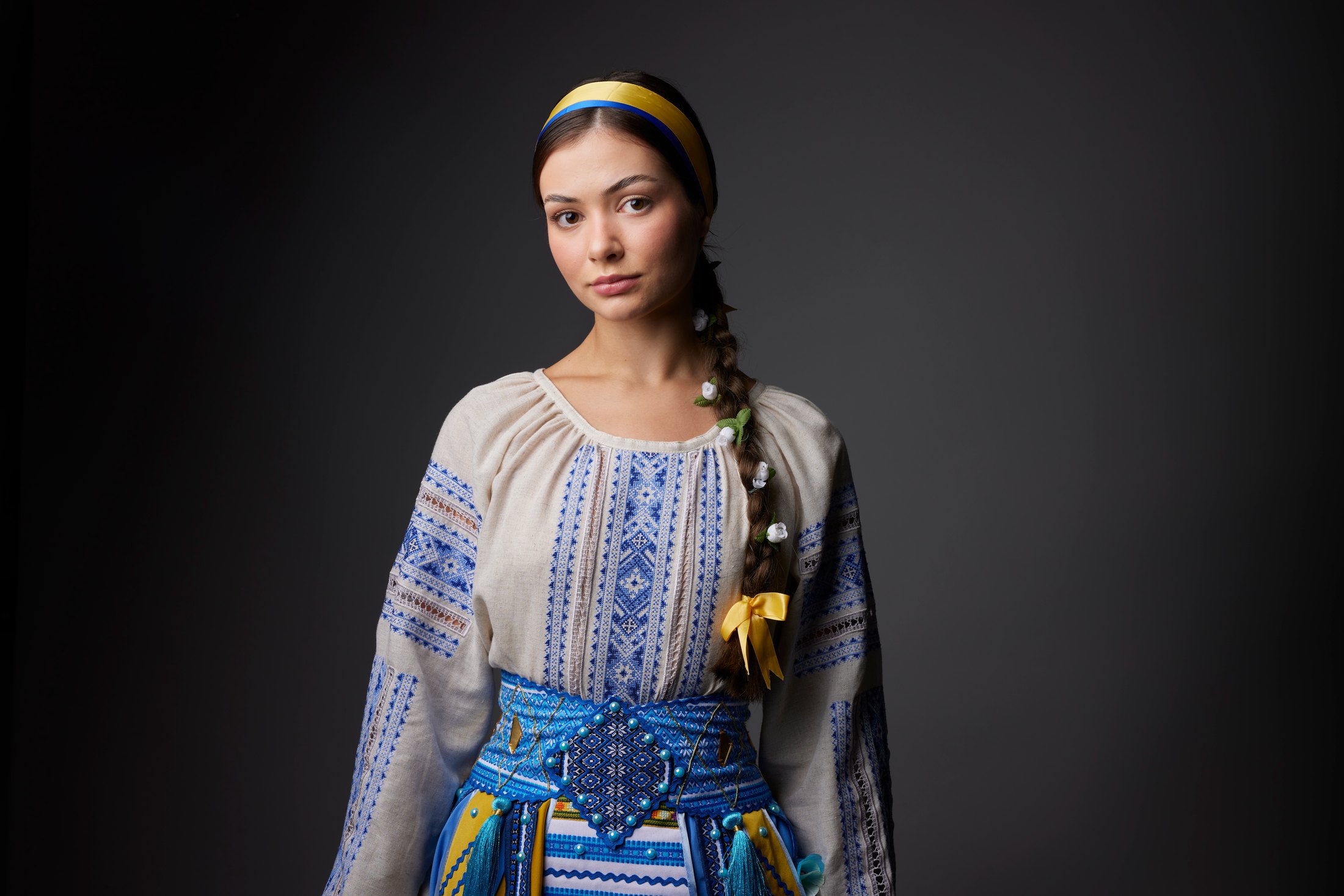 A dancer in a blue-embroidered blouse and headband, against grey