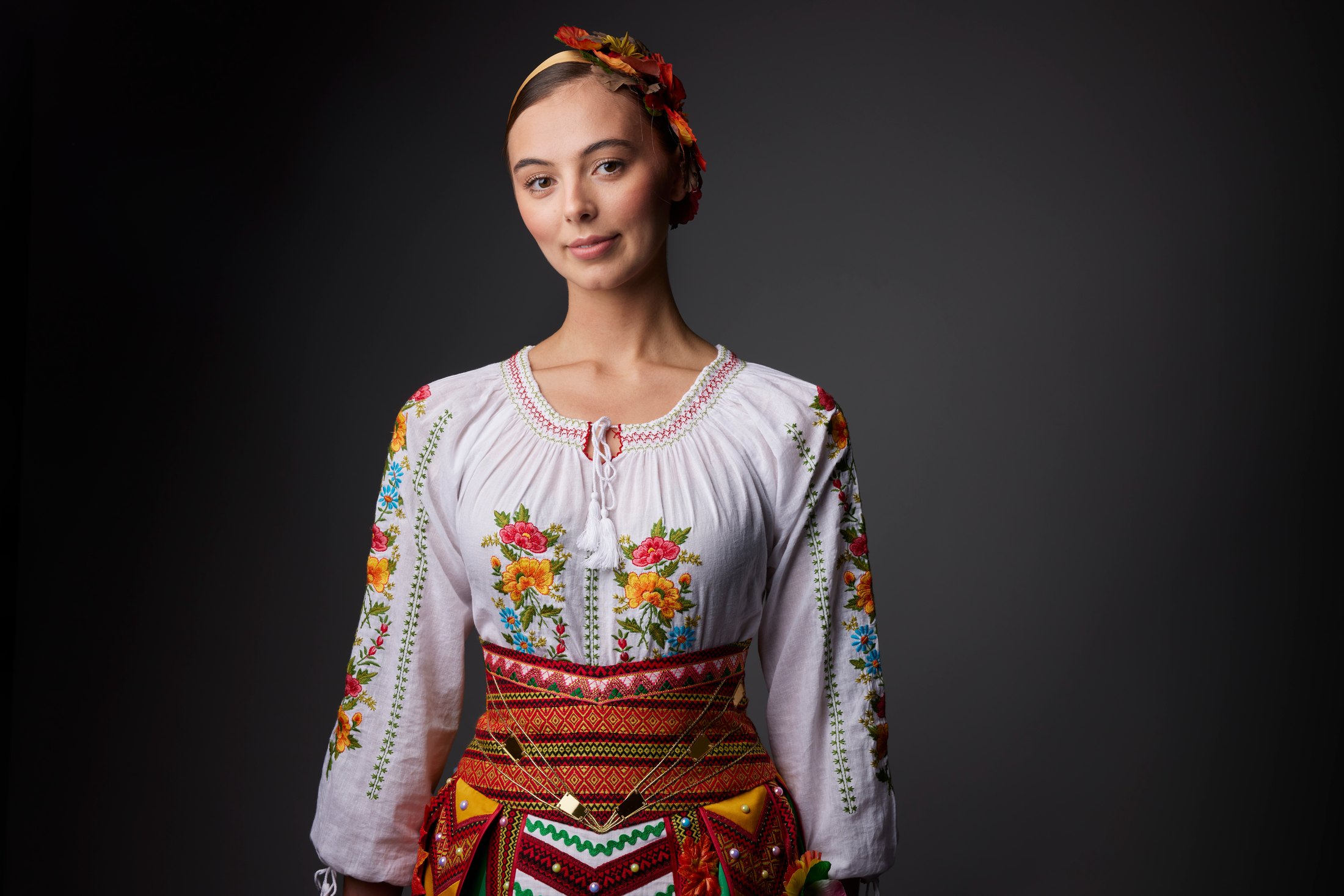 A dancer in a floral headpiece and red-embroidered blouse, against grey