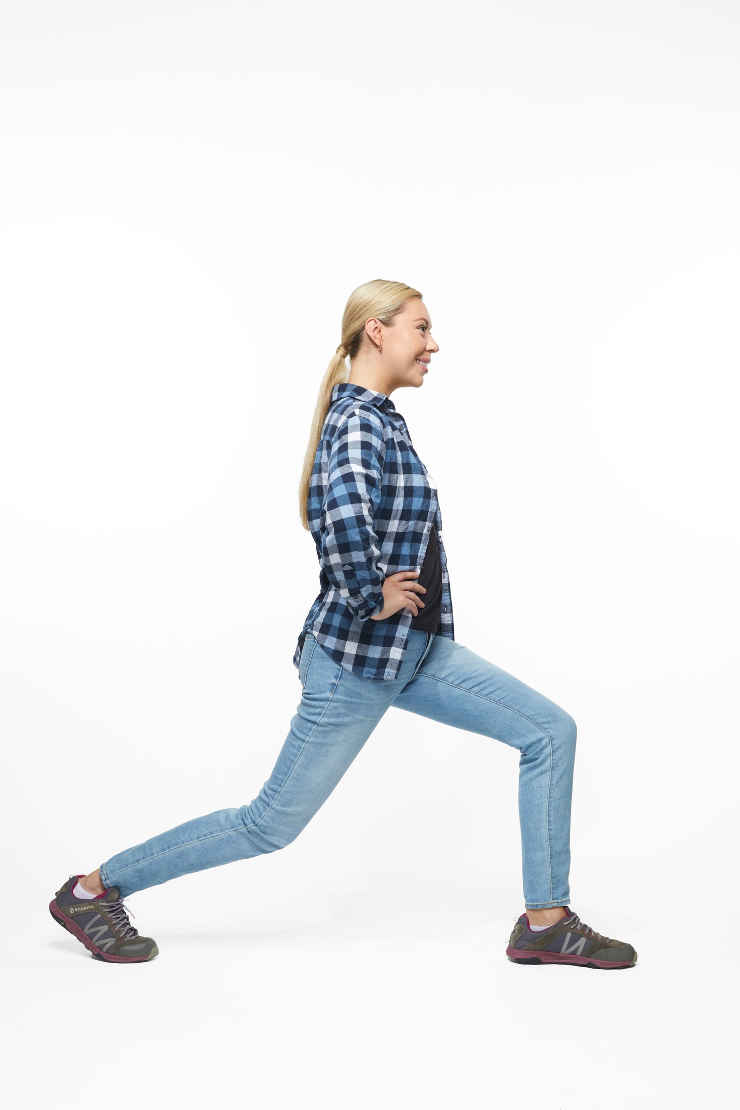 A woman in a plaid shirt and jeans in a lunge, full length on white