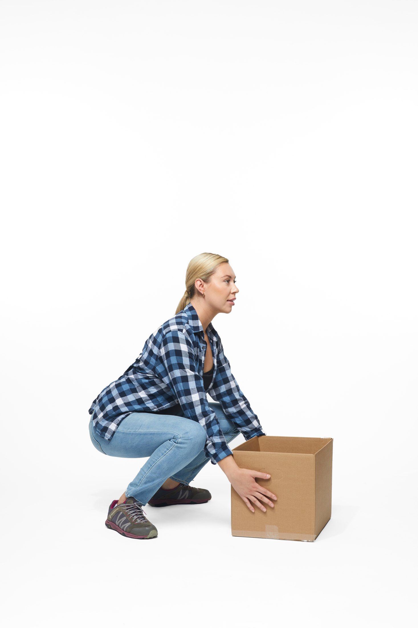 A woman in a plaid shirt and jeans lifting a box, full length on white