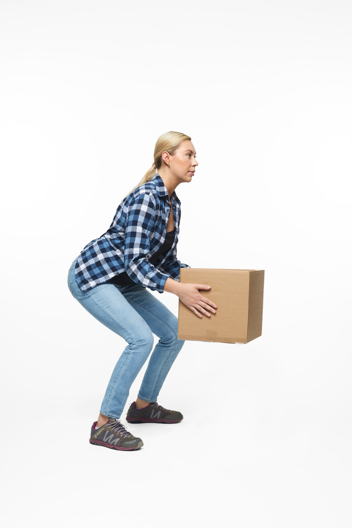 A woman in a plaid shirt and jeans lifting a box, full length on white