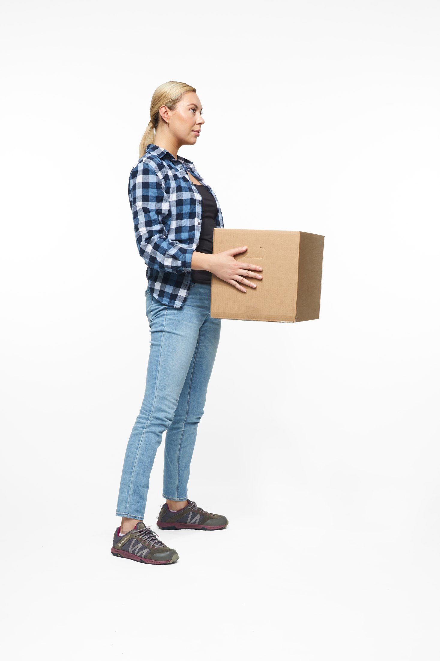 A woman in a plaid shirt and jeans lifting a box, full length on white