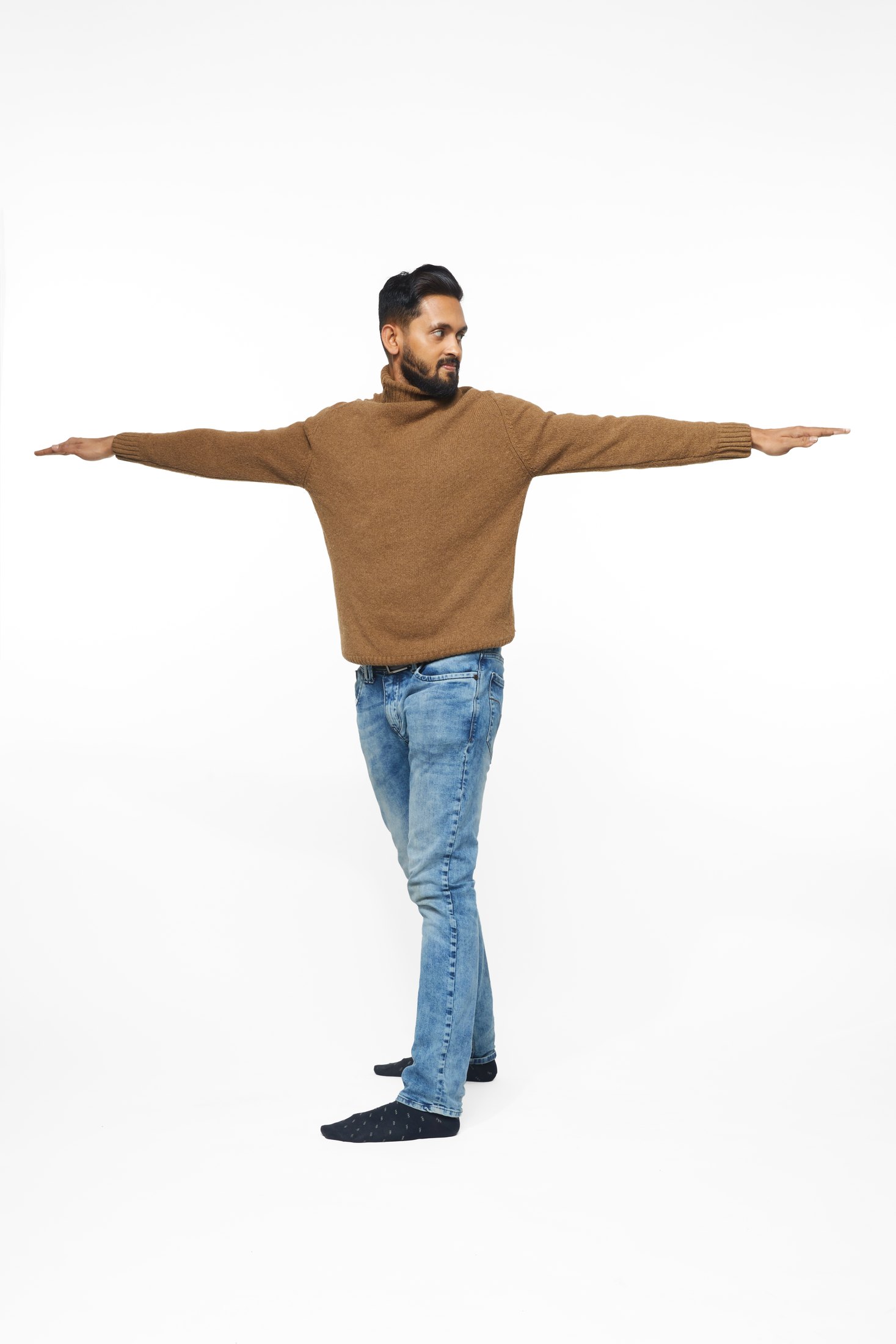 A man in a brown sweater and jeans in one of the program’s stretches, full length on white