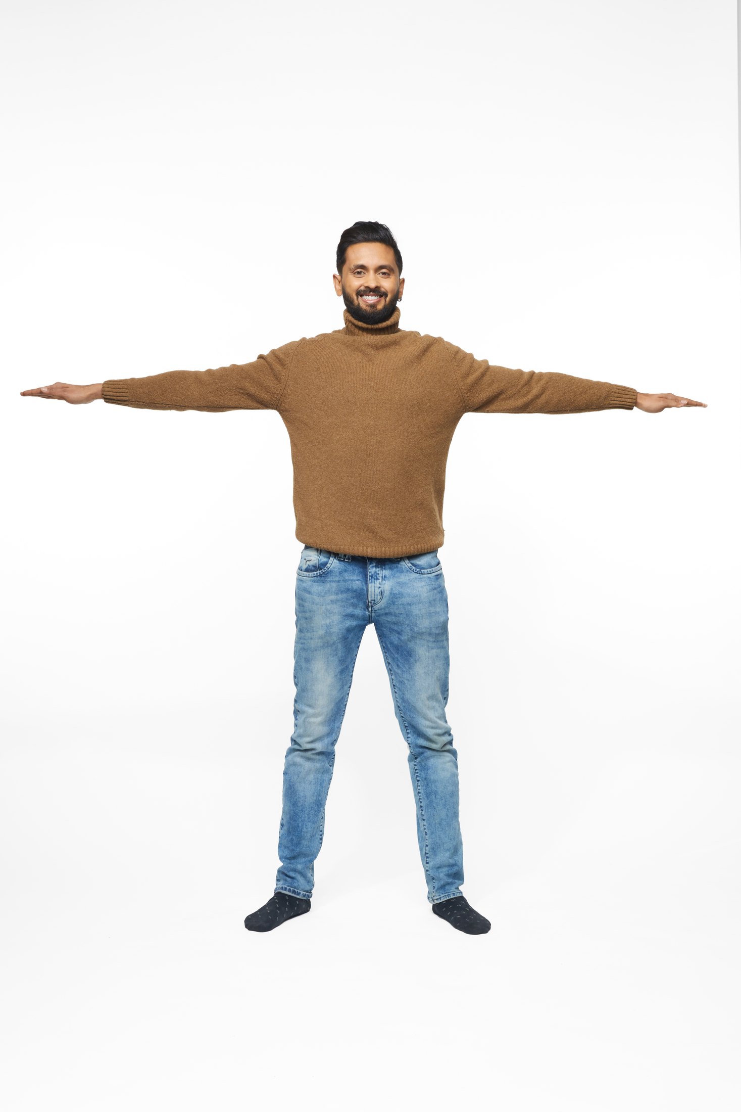 A man in a brown sweater and jeans in one of the program’s stretches, full length on white