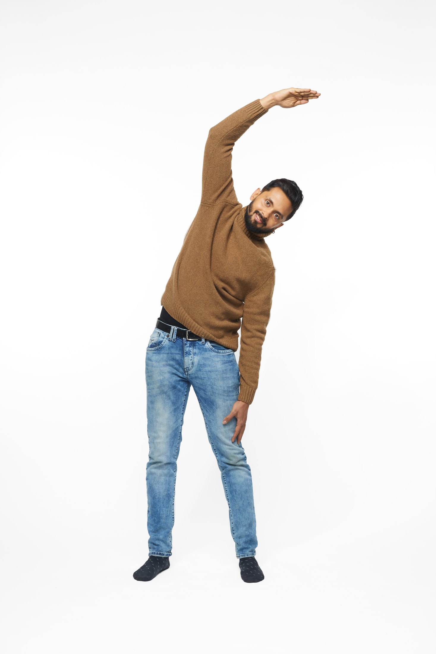 A man in a brown sweater and jeans in one of the program’s stretches, full length on white