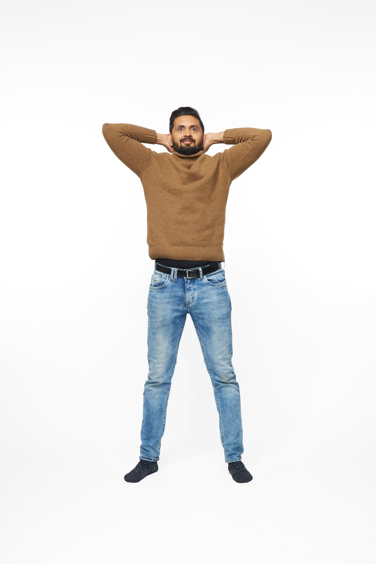 A man in a brown sweater and jeans in one of the program’s stretches, full length on white