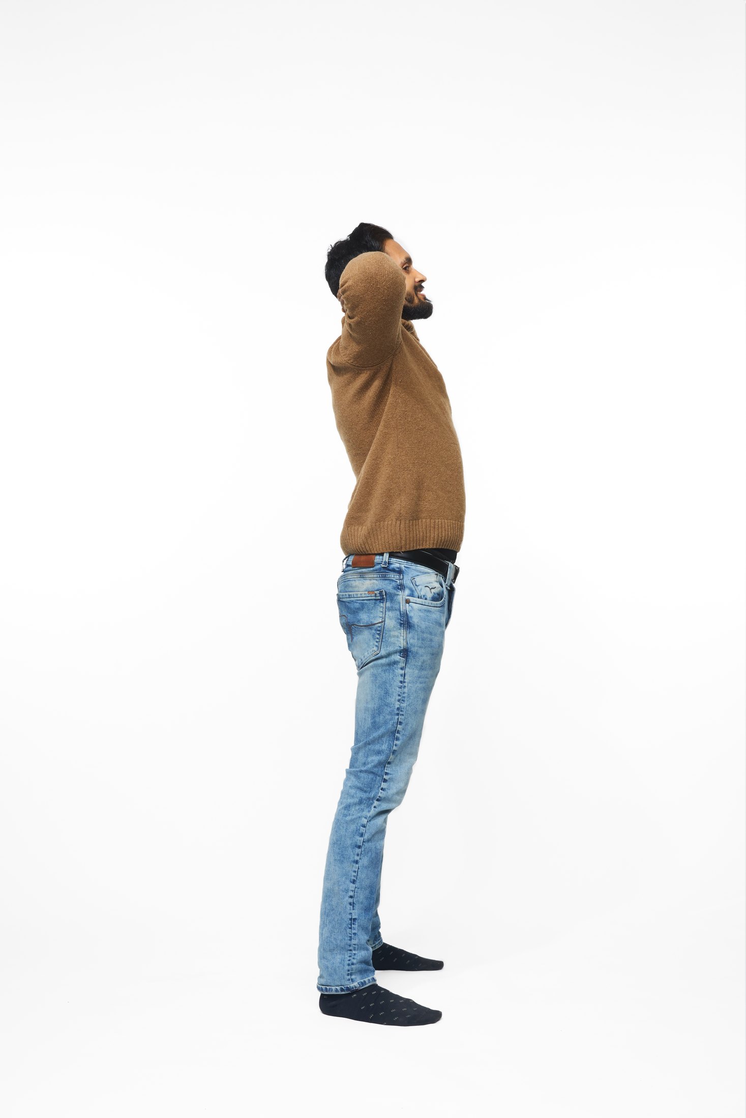 A man in a brown sweater and jeans in one of the program’s stretches, full length on white