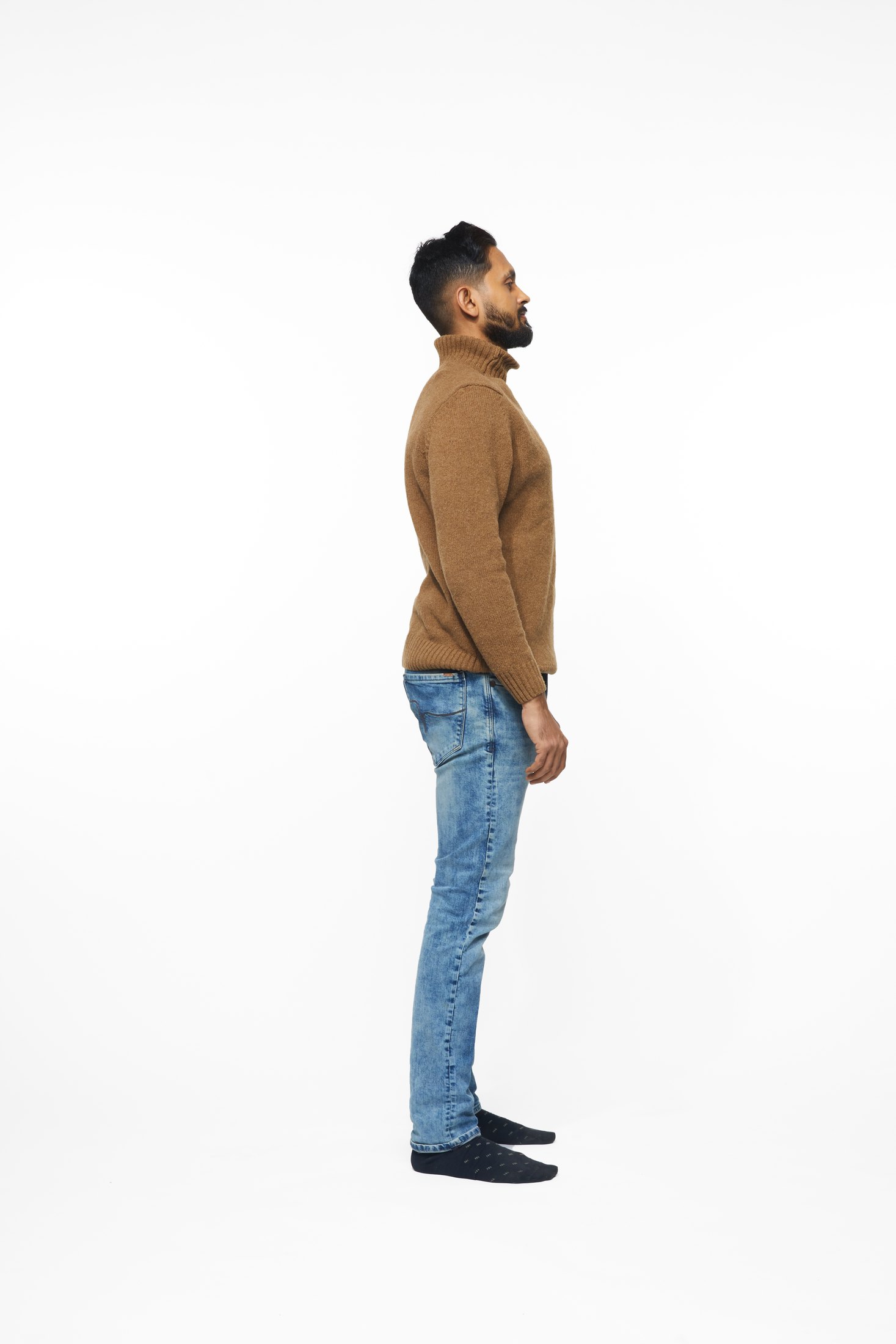 A man in a brown sweater and jeans in one of the program’s stretches, full length on white