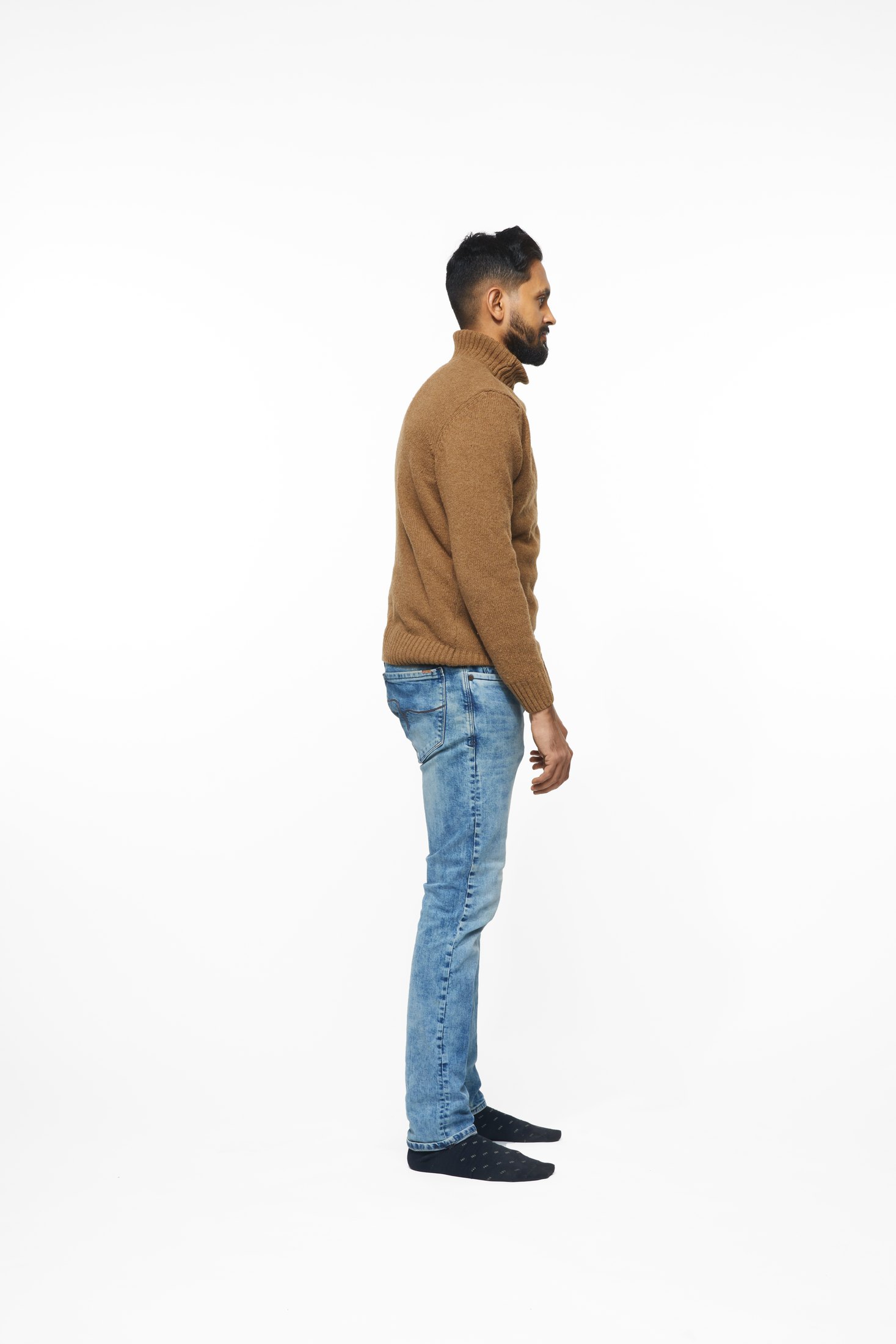 A man in a brown sweater and jeans in one of the program’s stretches, full length on white
