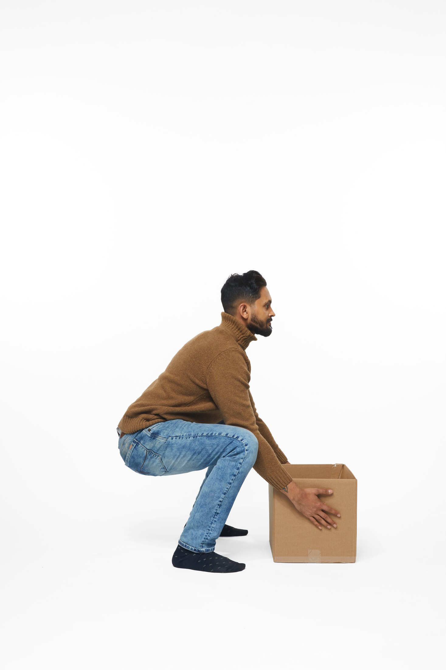 A man in a brown sweater and jeans lifting a box, full length on white
