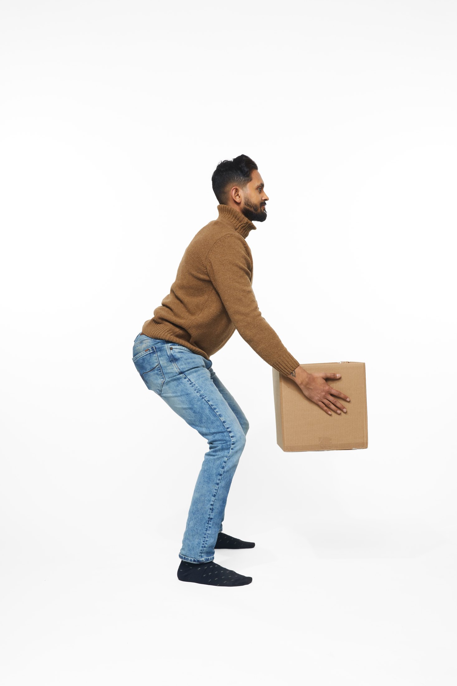 A man in a brown sweater and jeans lifting a box, full length on white