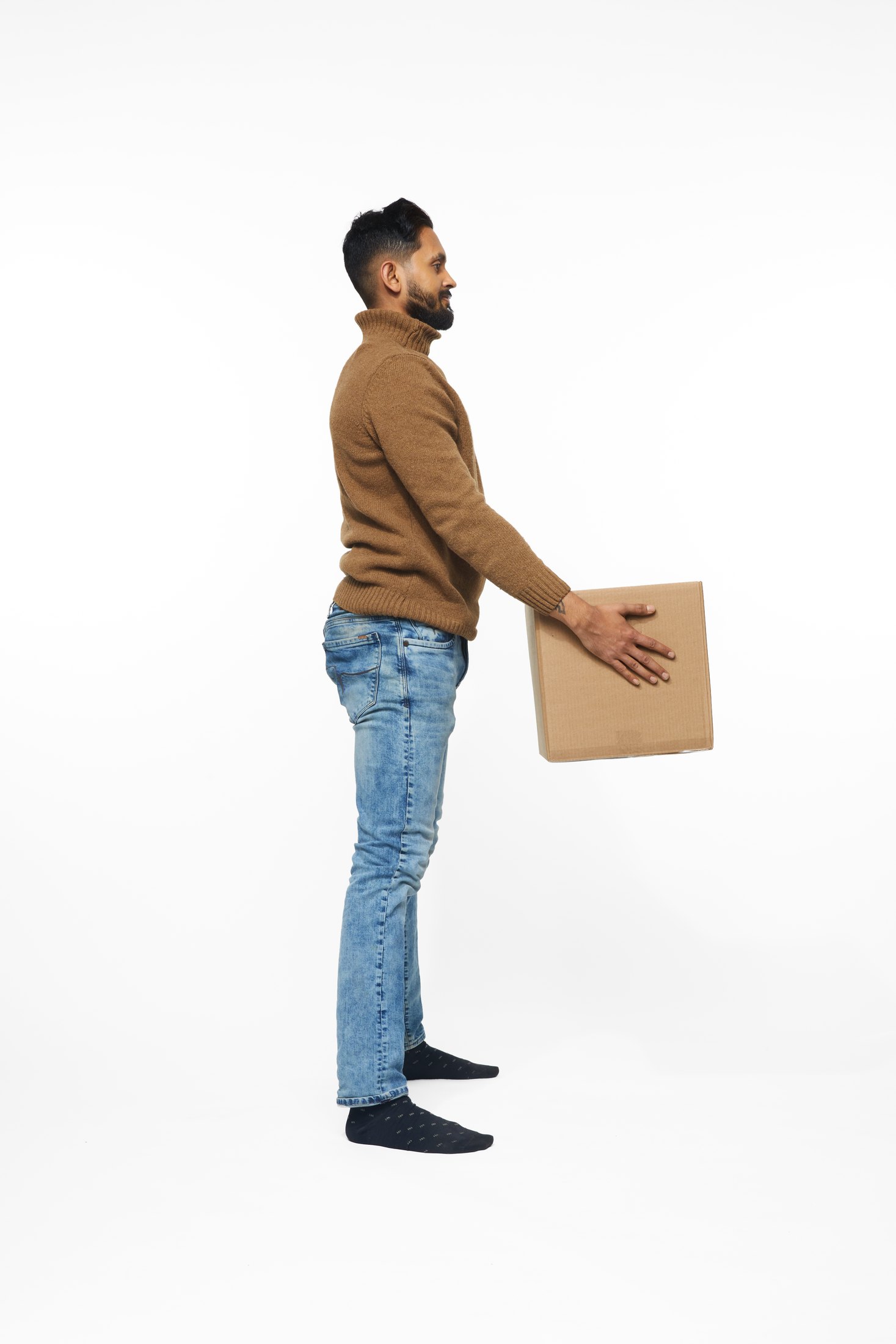 A man in a brown sweater and jeans lifting a box, full length on white