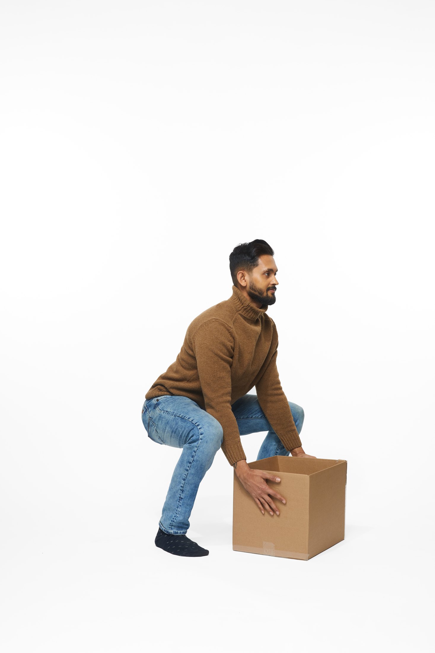 A man in a brown sweater and jeans lifting a box, full length on white