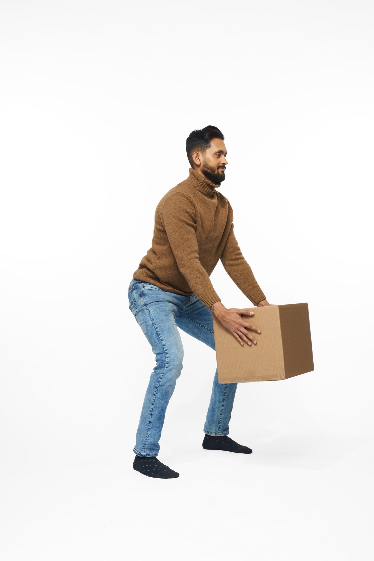 A man in a brown sweater and jeans lifting a box, full length on white
