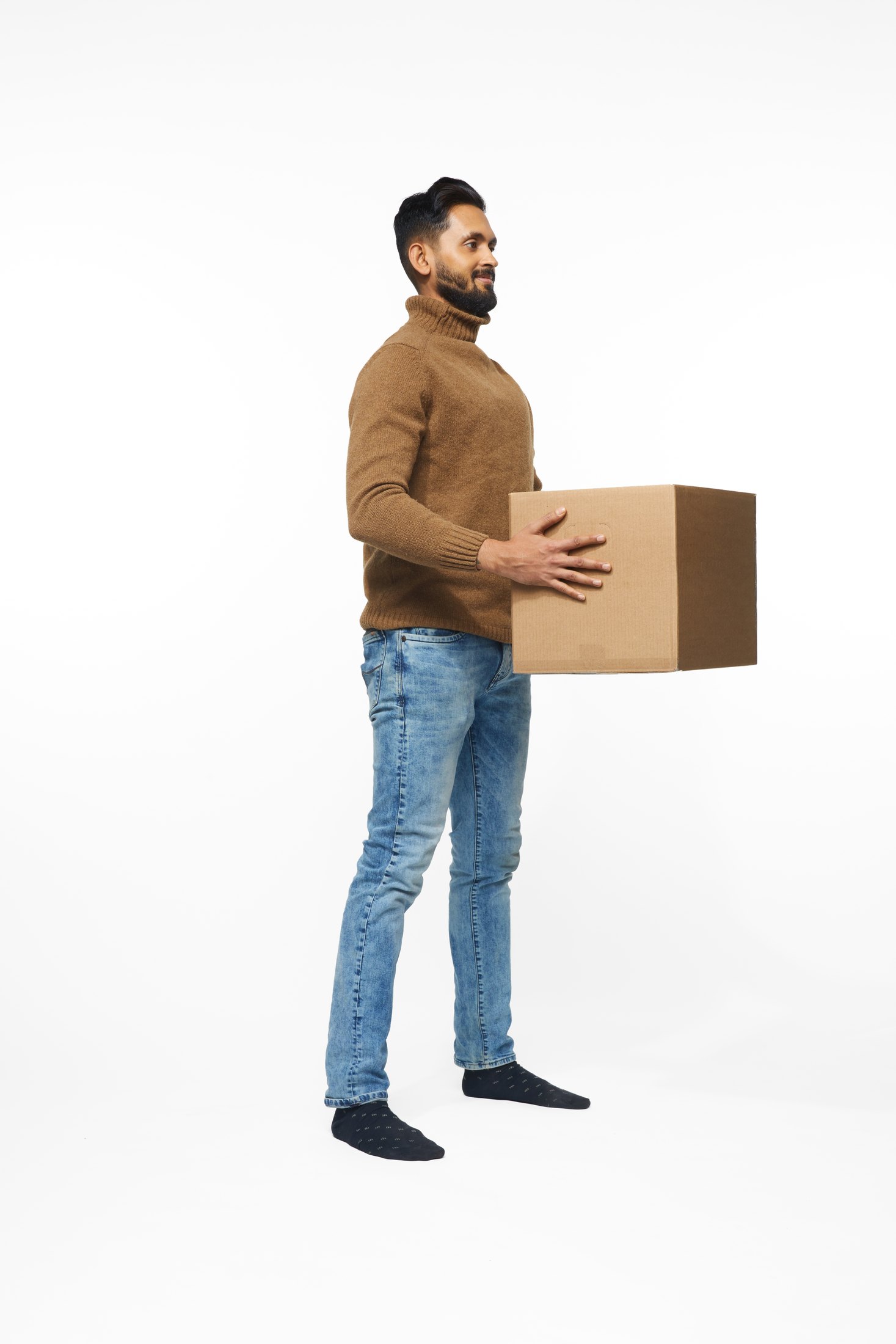 A man in a brown sweater and jeans lifting a box, full length on white
