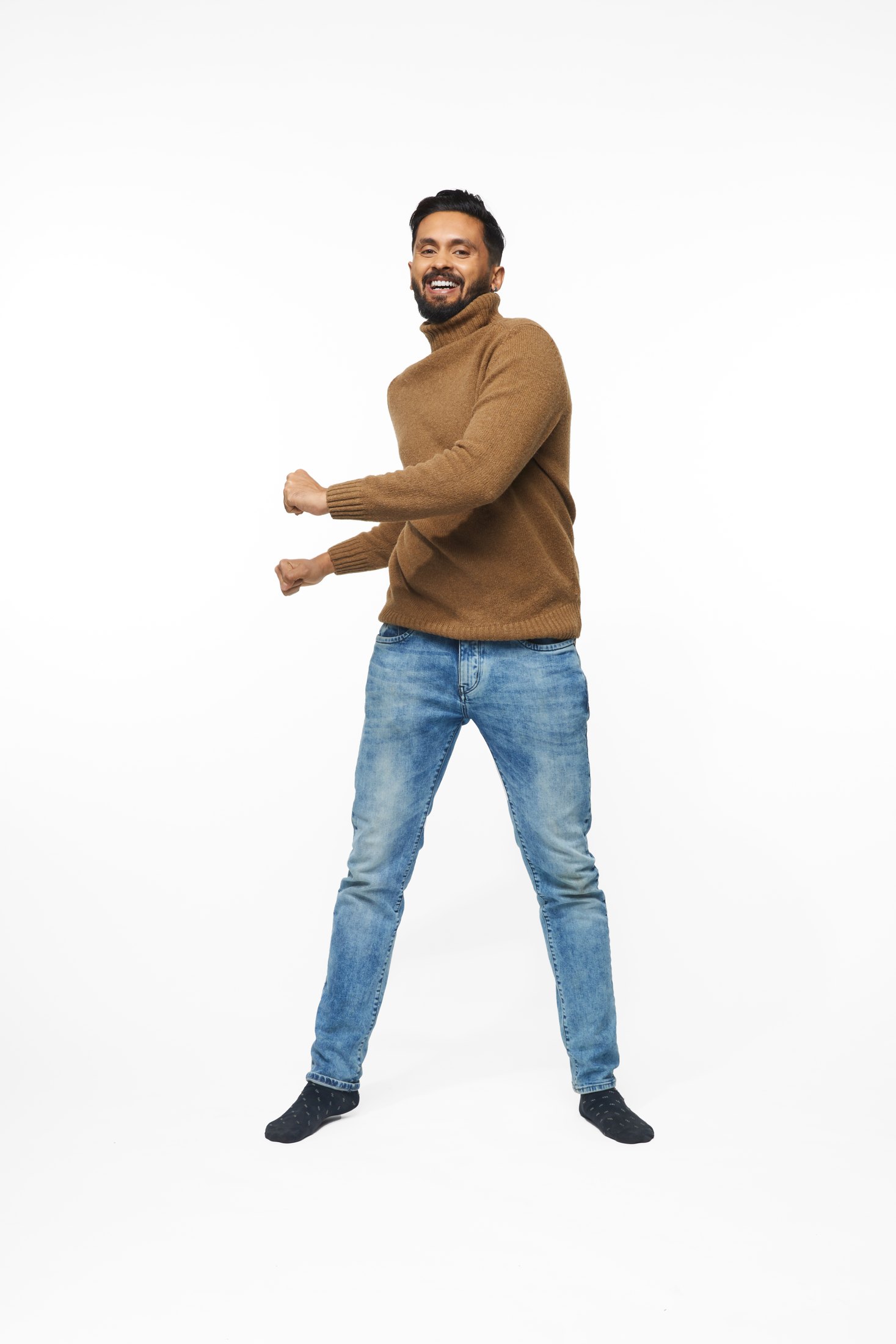 A man in a brown sweater and jeans in one of the program’s stretches, full length on white