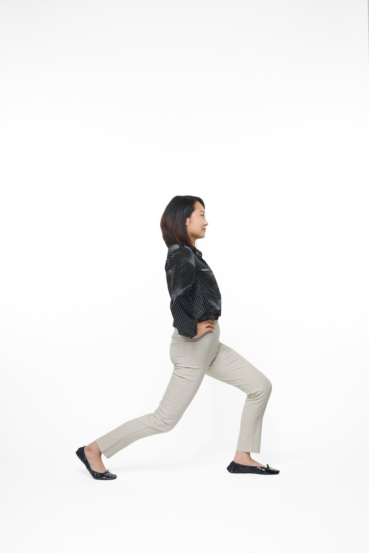 A woman in a black jacket and pale trousers in a lunge, full length on white