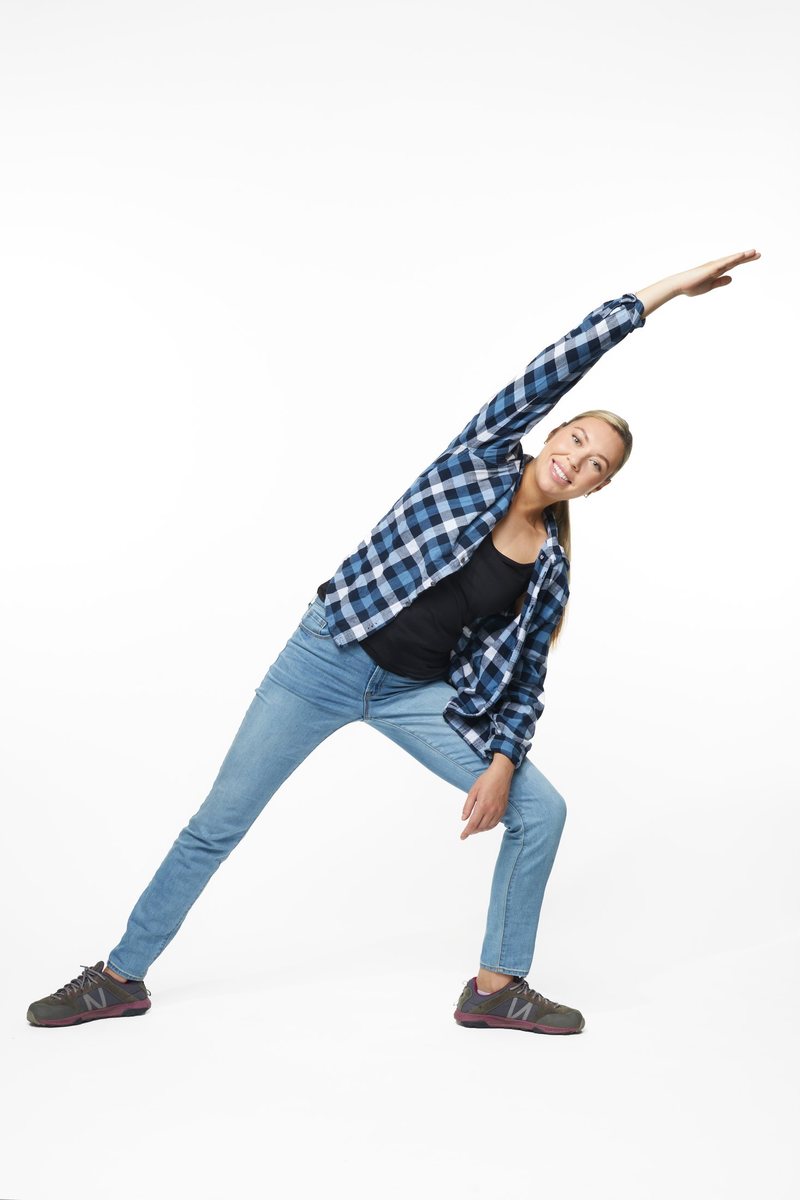 A woman in a plaid shirt and jeans in one of the program’s stretches, full length on white
