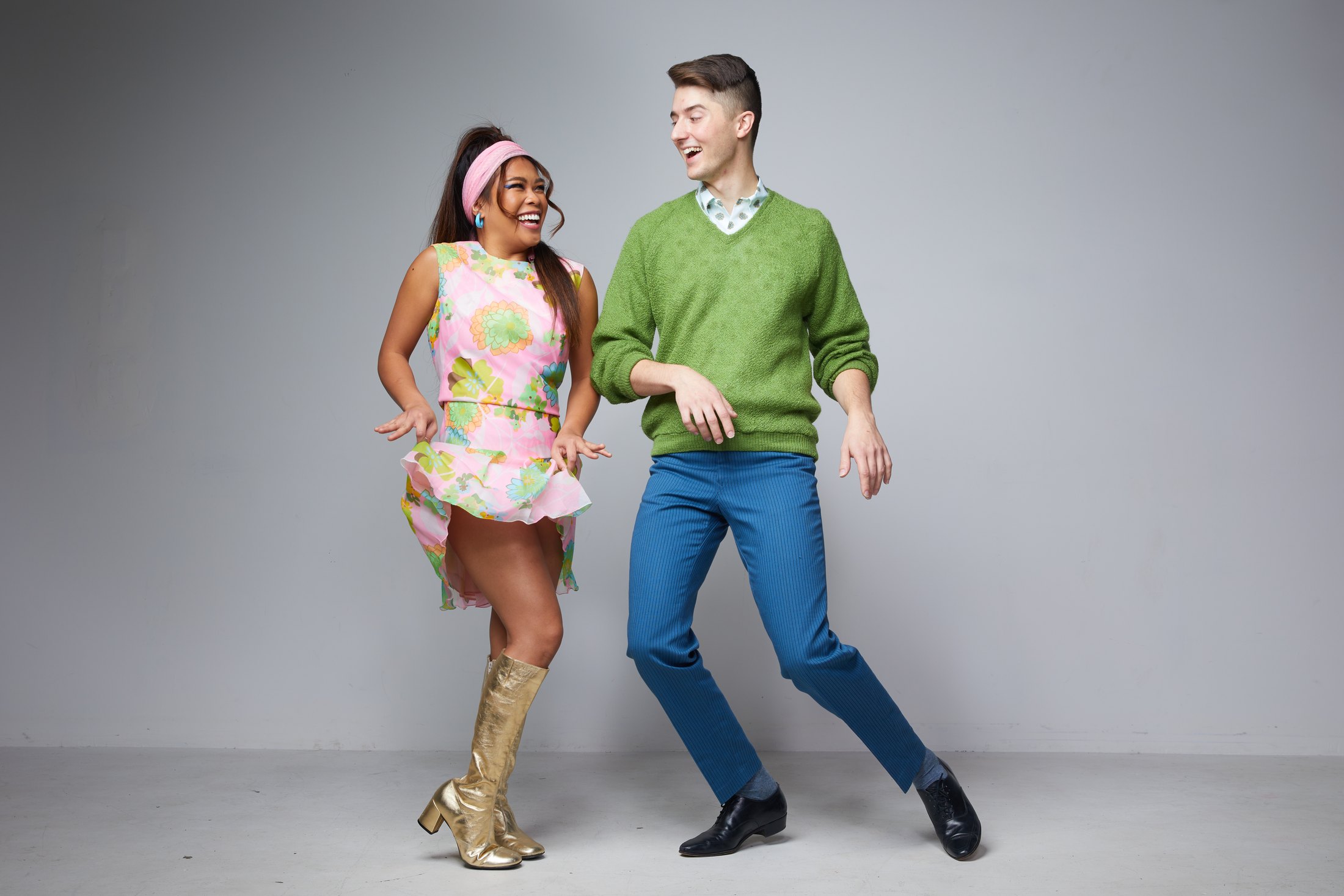 Two performers dancing, a pink print minidress and gold boots beside a green sweater, against grey