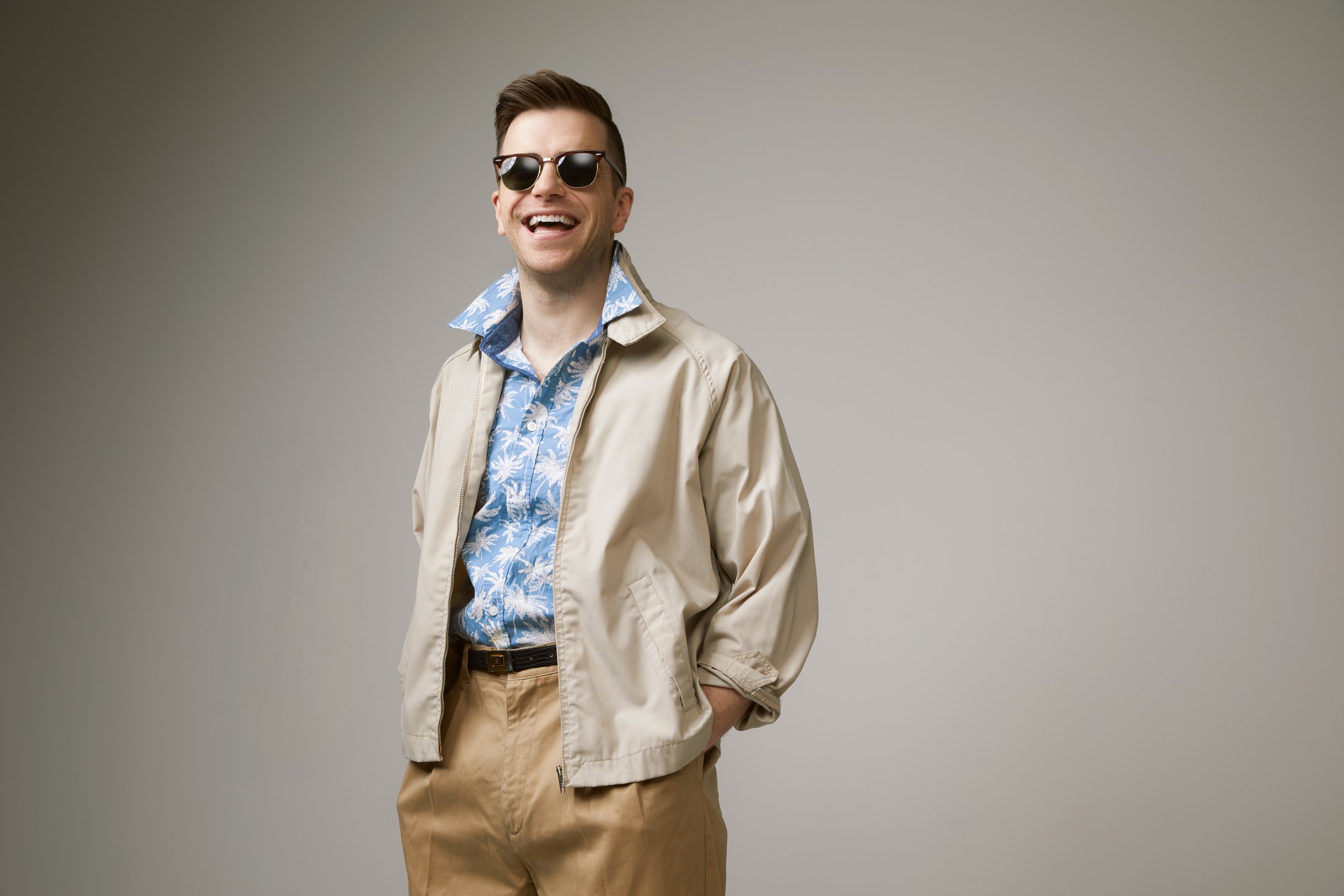 The same performer in his sunglasses, smiling, against grey