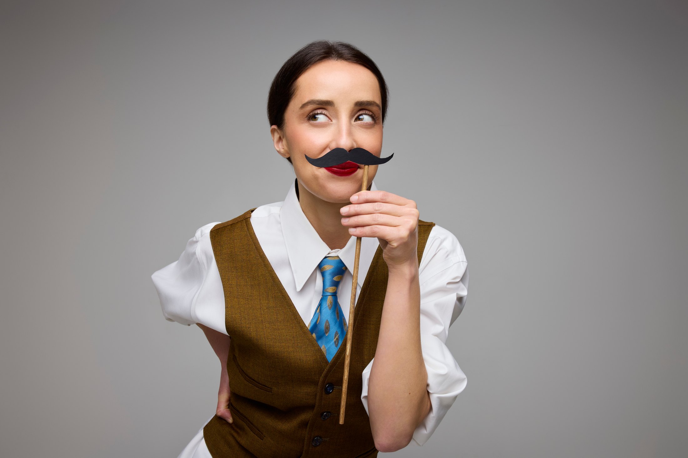A performer in a waistcoat and tie behind a moustache on a stick