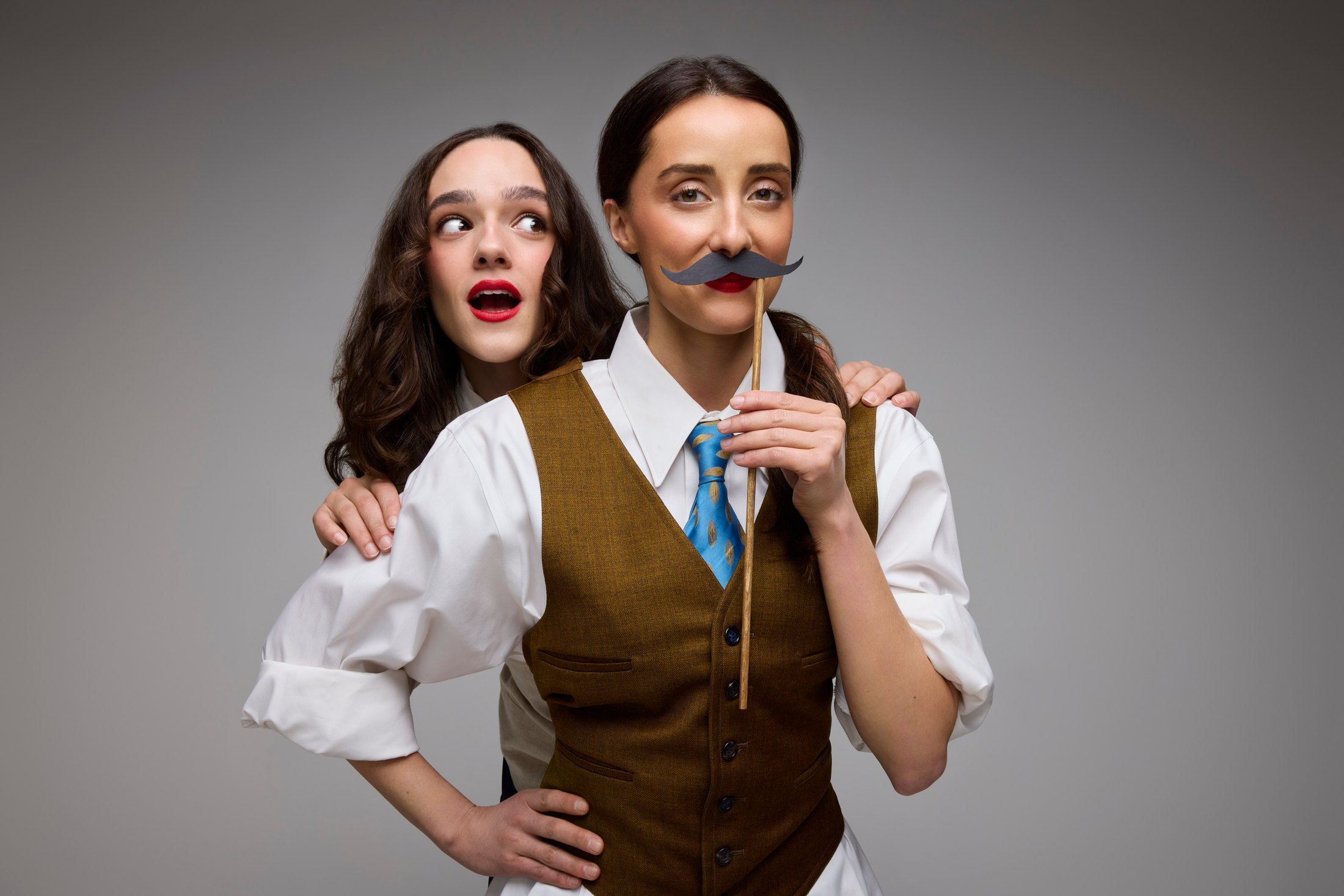 Two performers in waistcoat and blouse, one holding a moustache on a stick