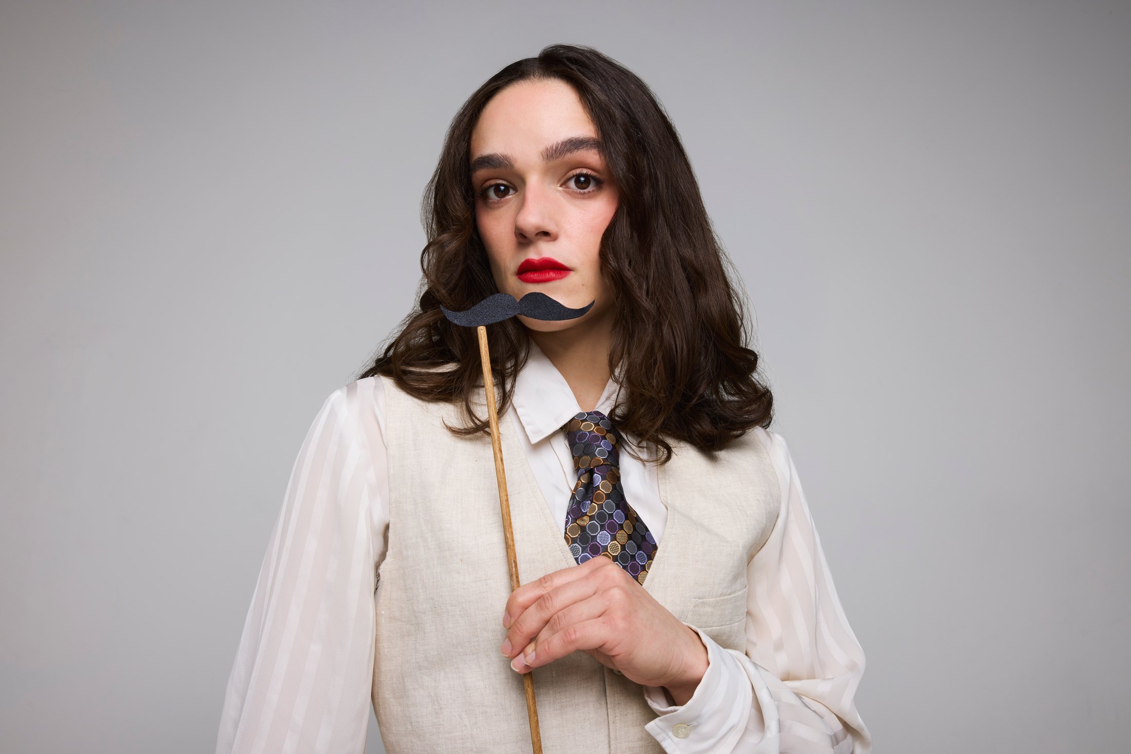 A performer in a white blouse and loose tie, a prop held to her mouth
