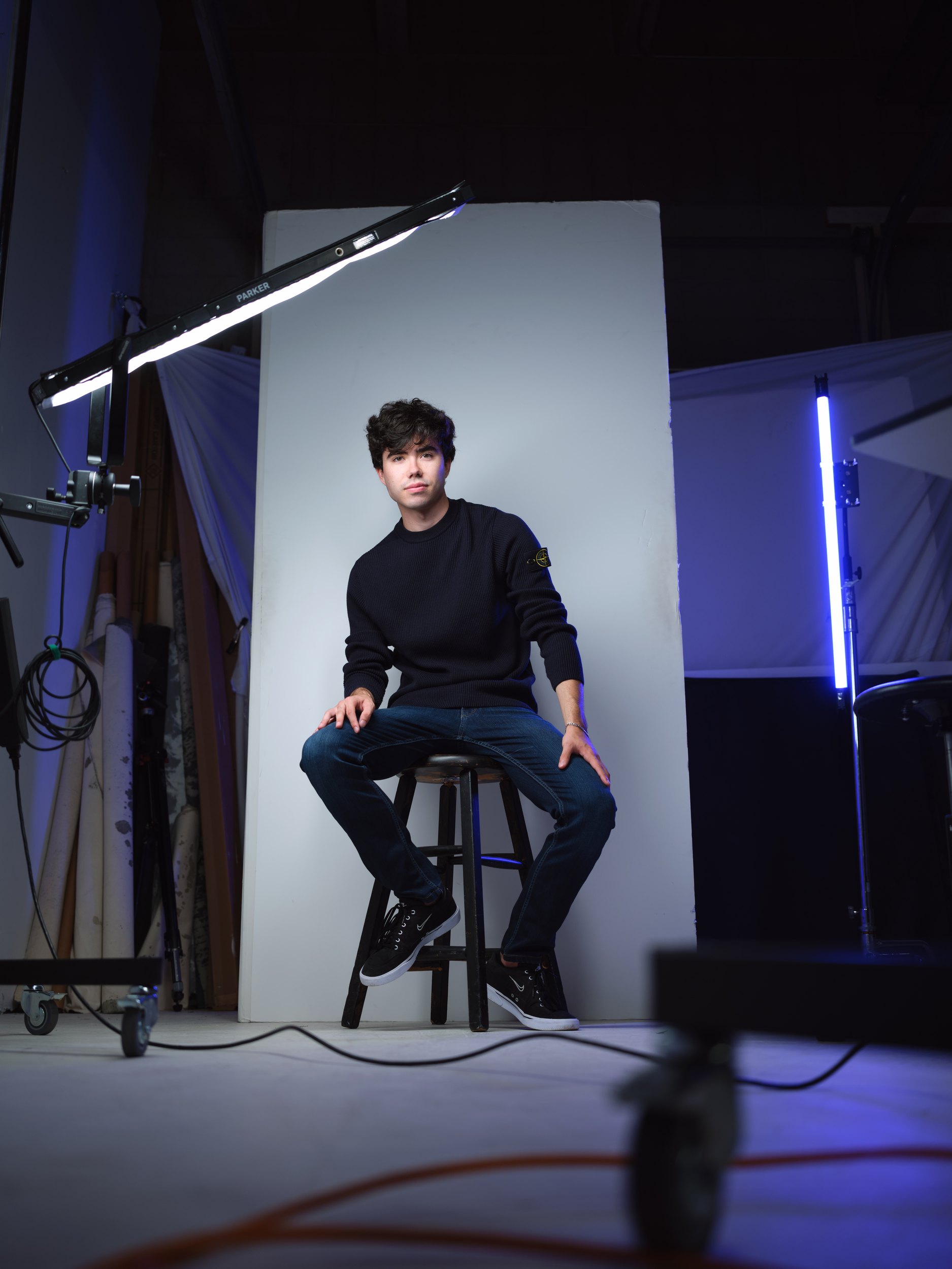The same session, seated on a stool on the set with the lights and a blue tube left in the shot
