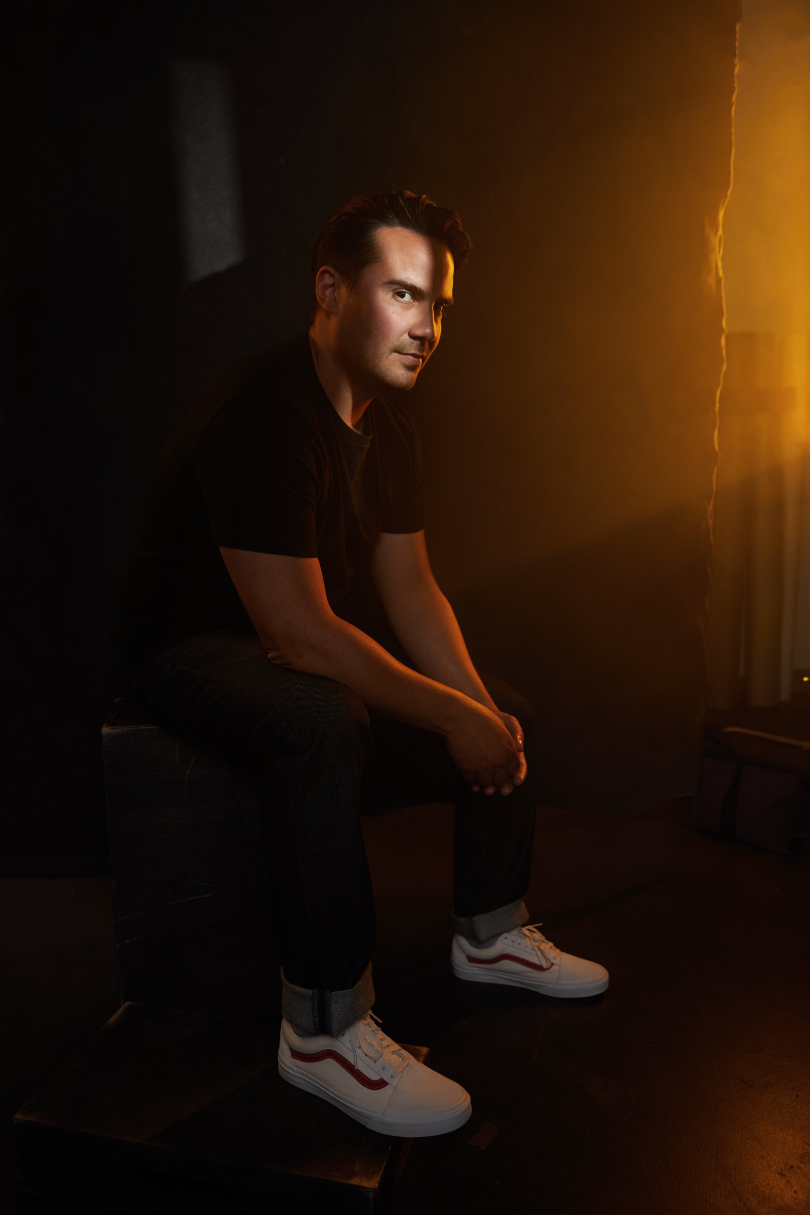 The same session, seated on a box in warm amber light, white sneakers