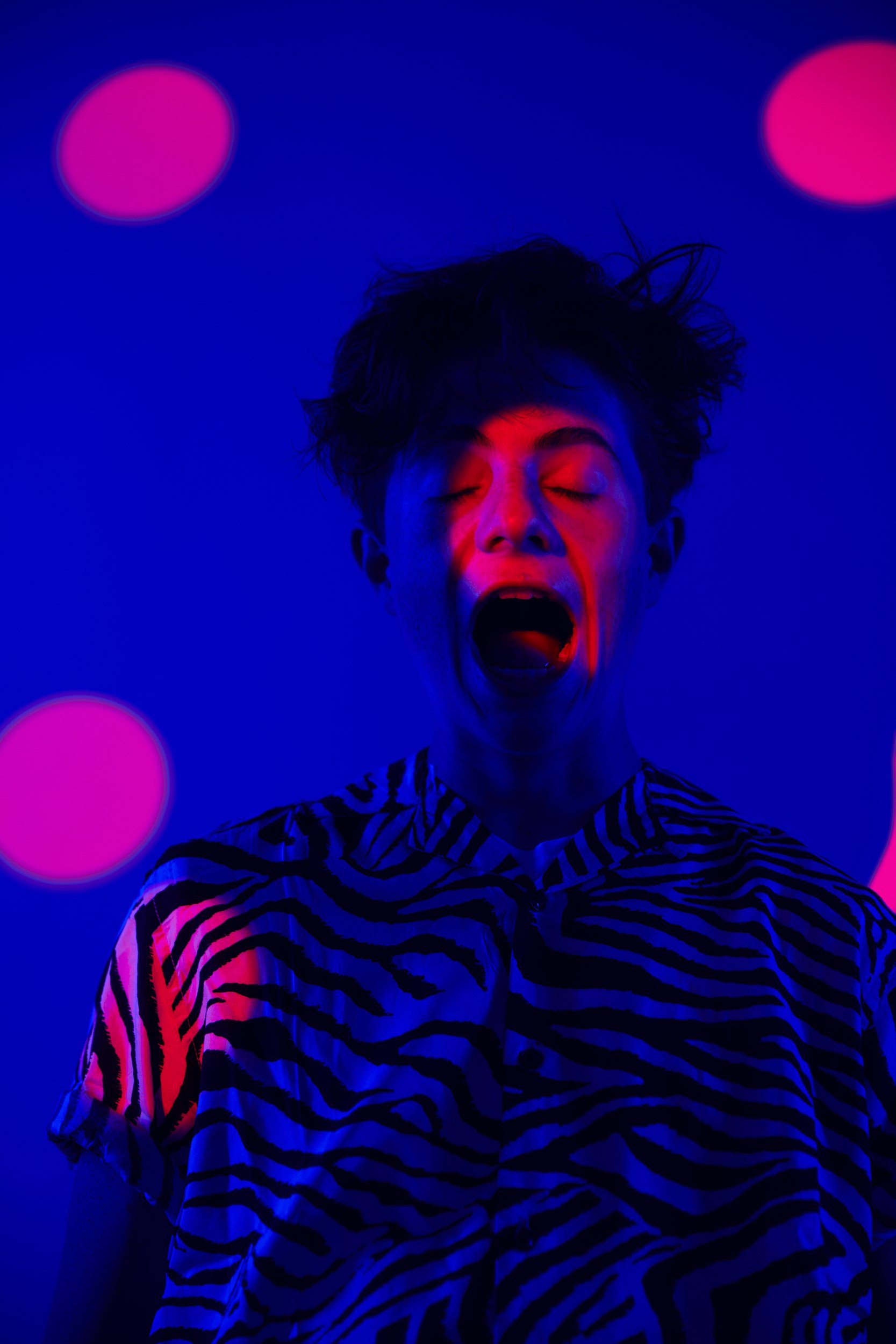 Content creator portrait: a zebra-print shirt under blue and pink light, mid-shout
