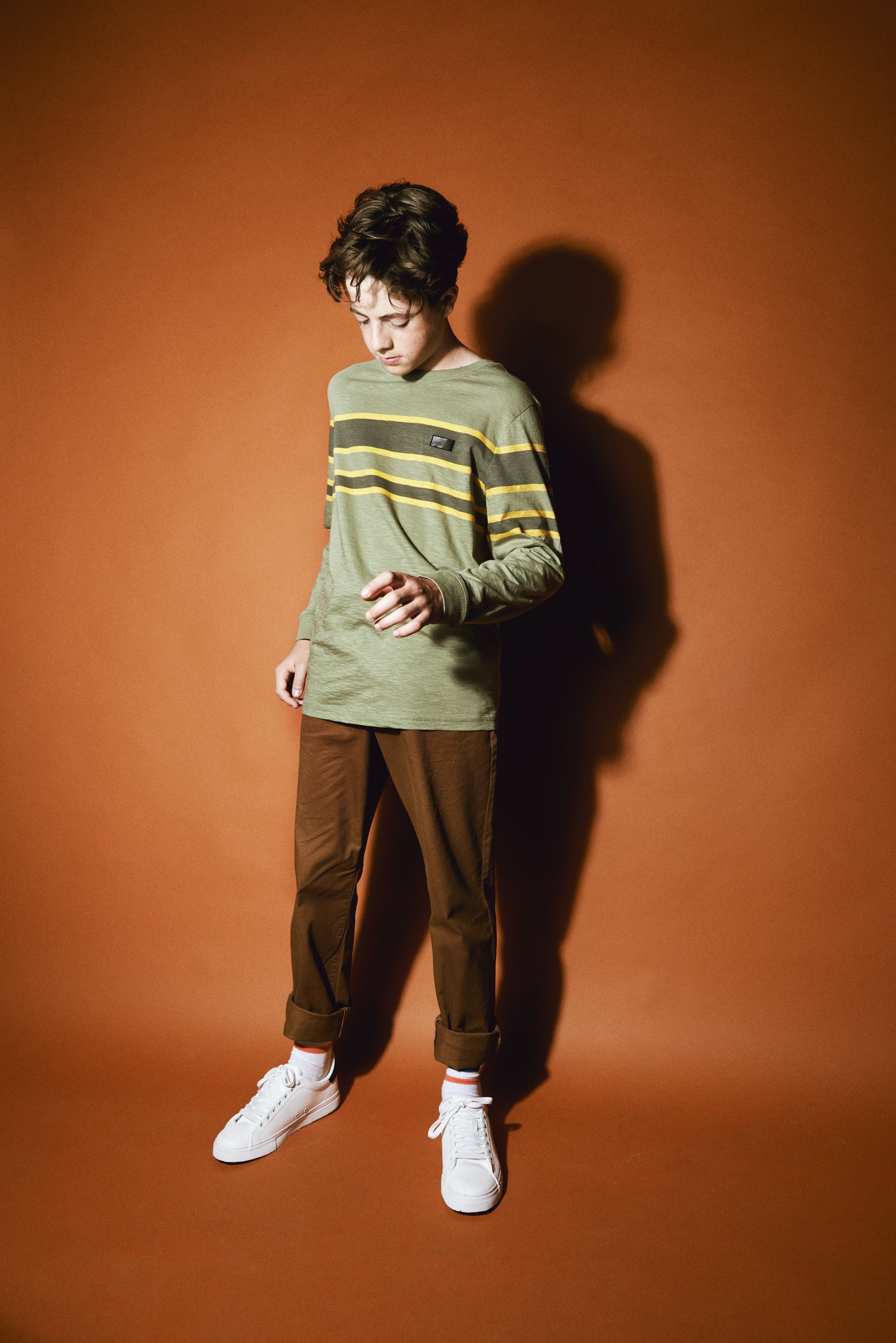 A striped green sweater and brown trousers against rust, head to toe