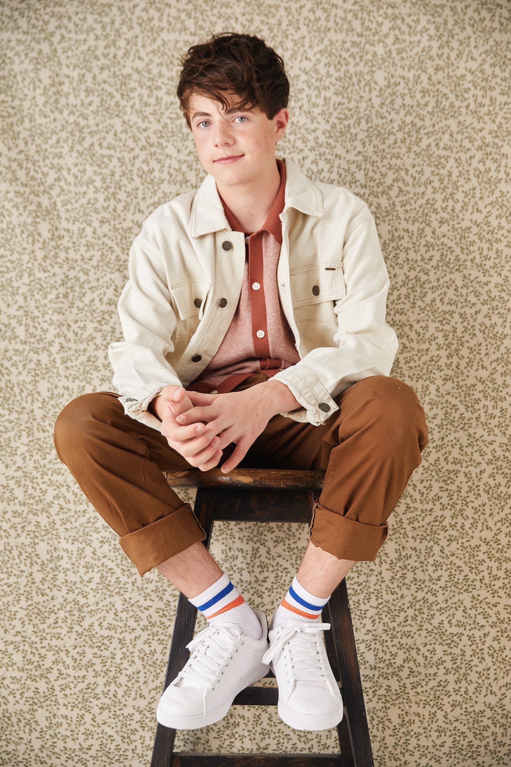 The cream jacket, seated on a stool against the floral backdrop